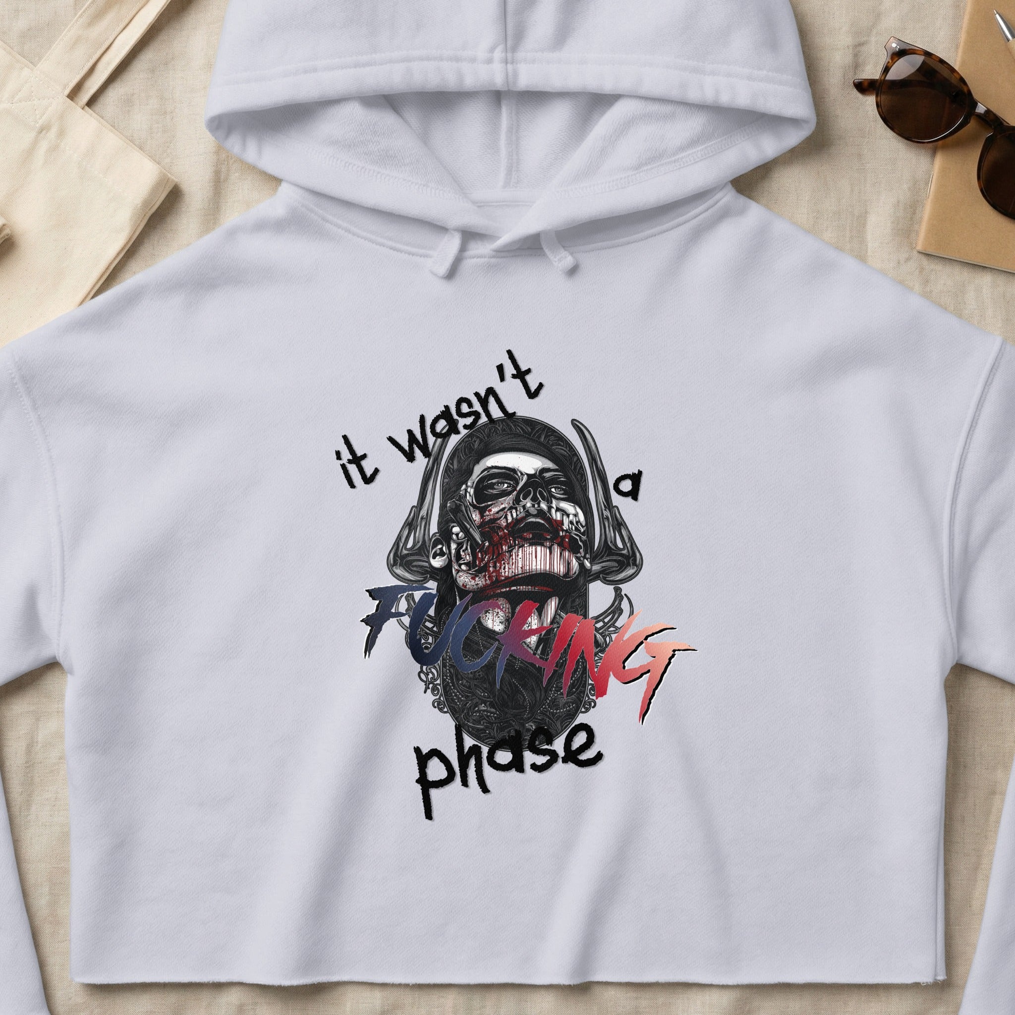 White cropped hoodie with "it wasn't a fucking phase" text and skull graphic.
