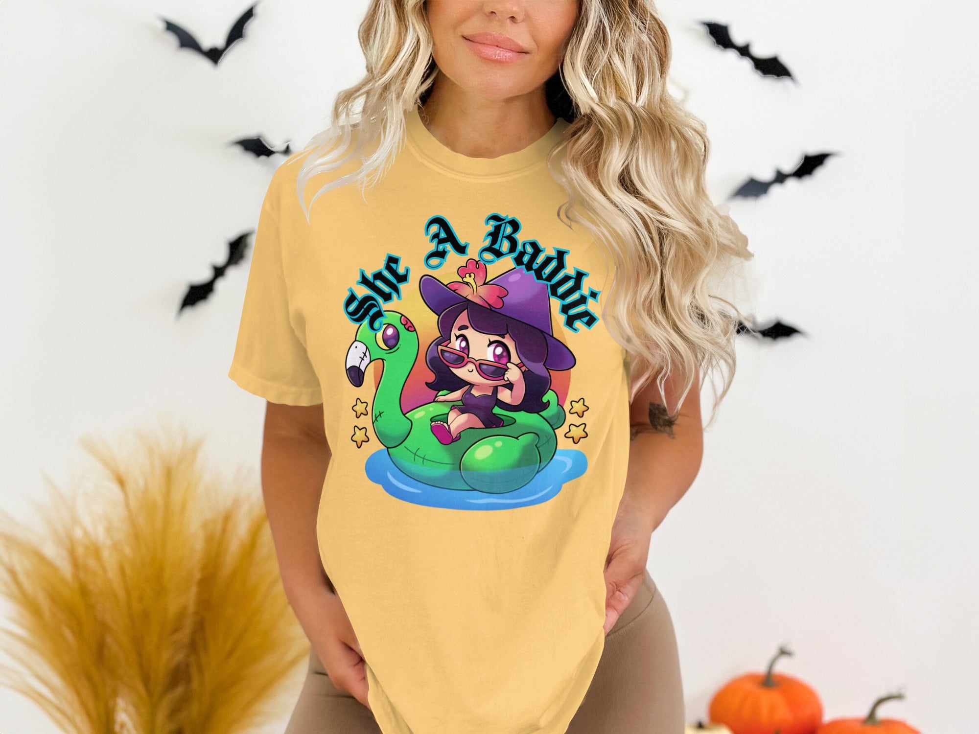 Yellow t-shirt with cartoon witch on flamingo float and text "she A Baddie".