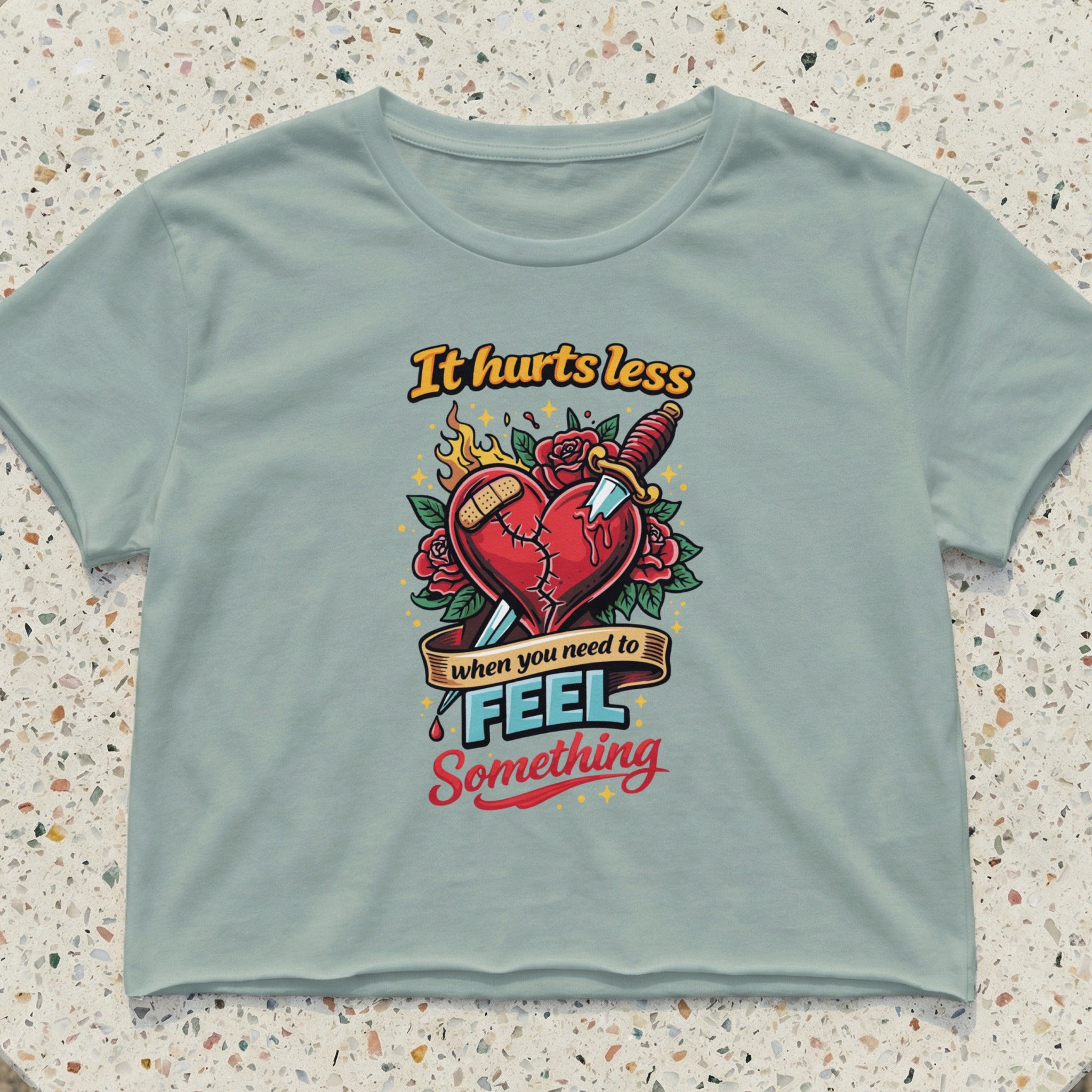 Light blue cropped t-shirt with "It hurts less when you need to feel something" text and heart graphic.