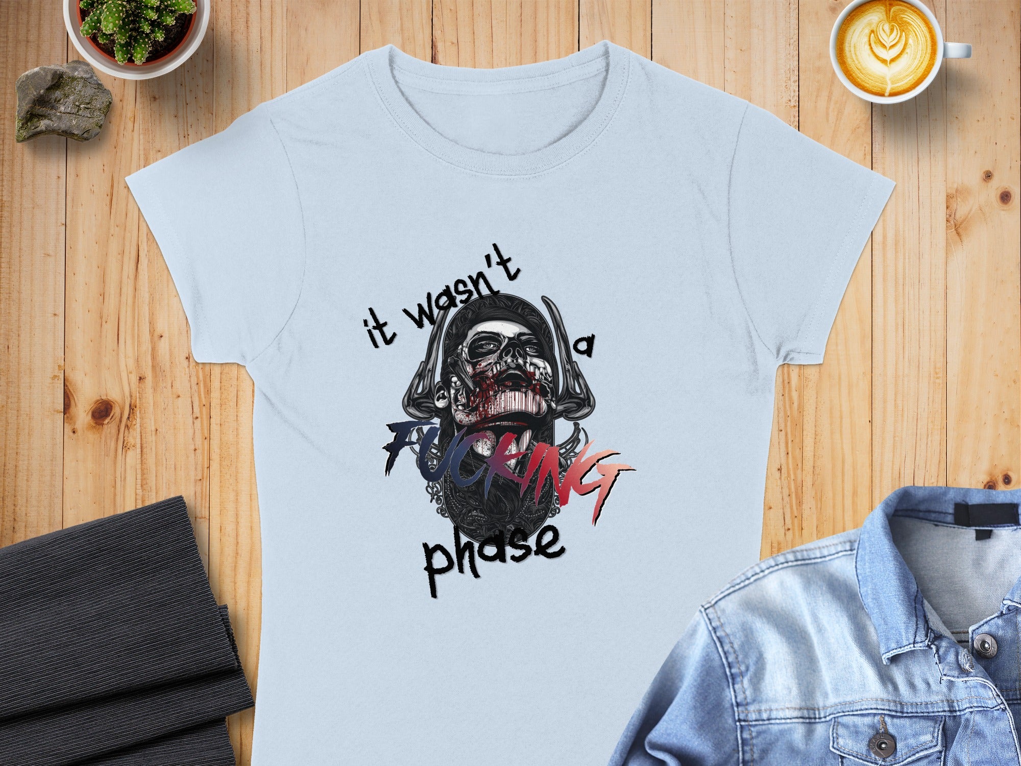 Light blue t-shirt with a skull graphic and "it wasn't a fucking phase" text.