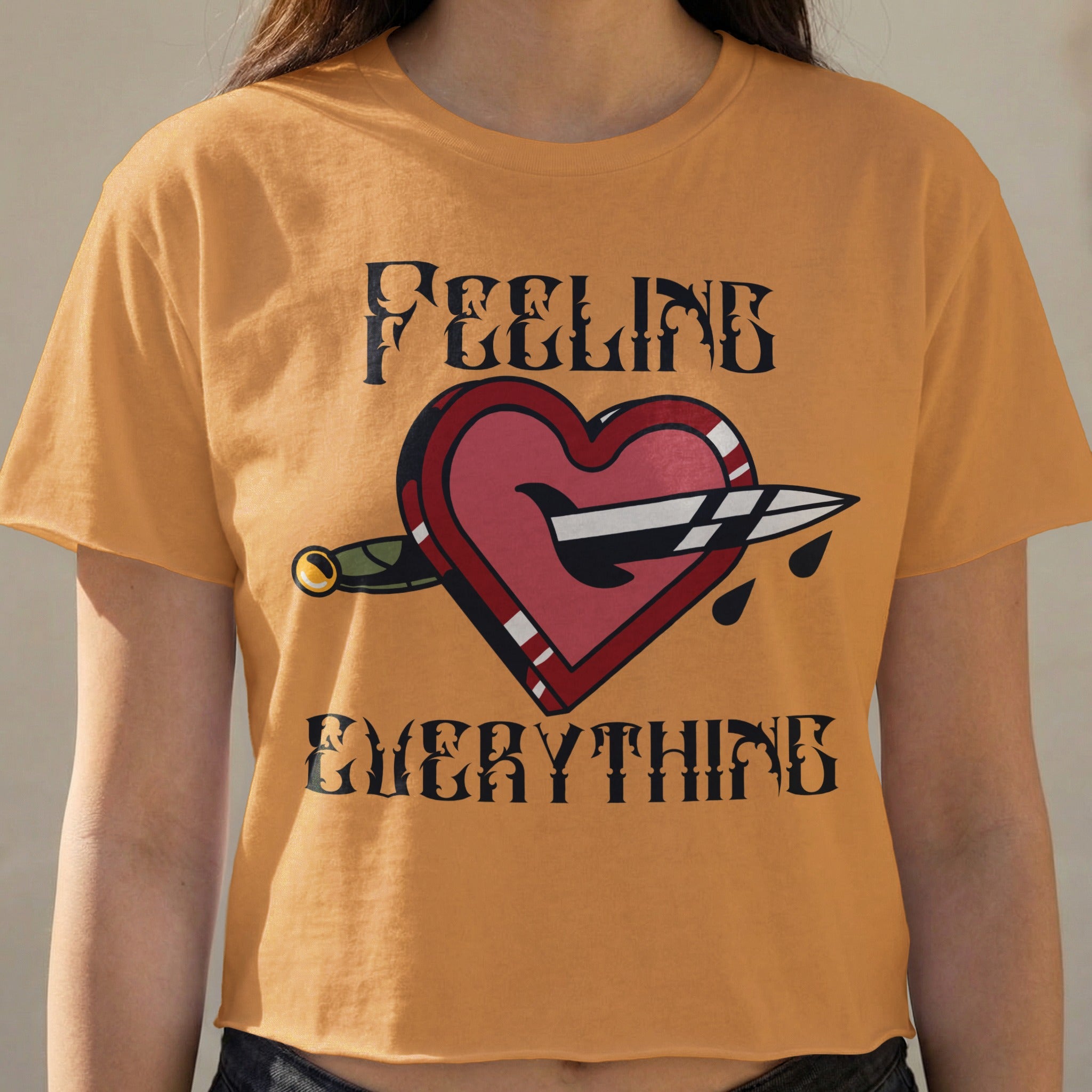 Orange t-shirt with dagger piercing heart graphic and text "FEELING EVERYTHING".