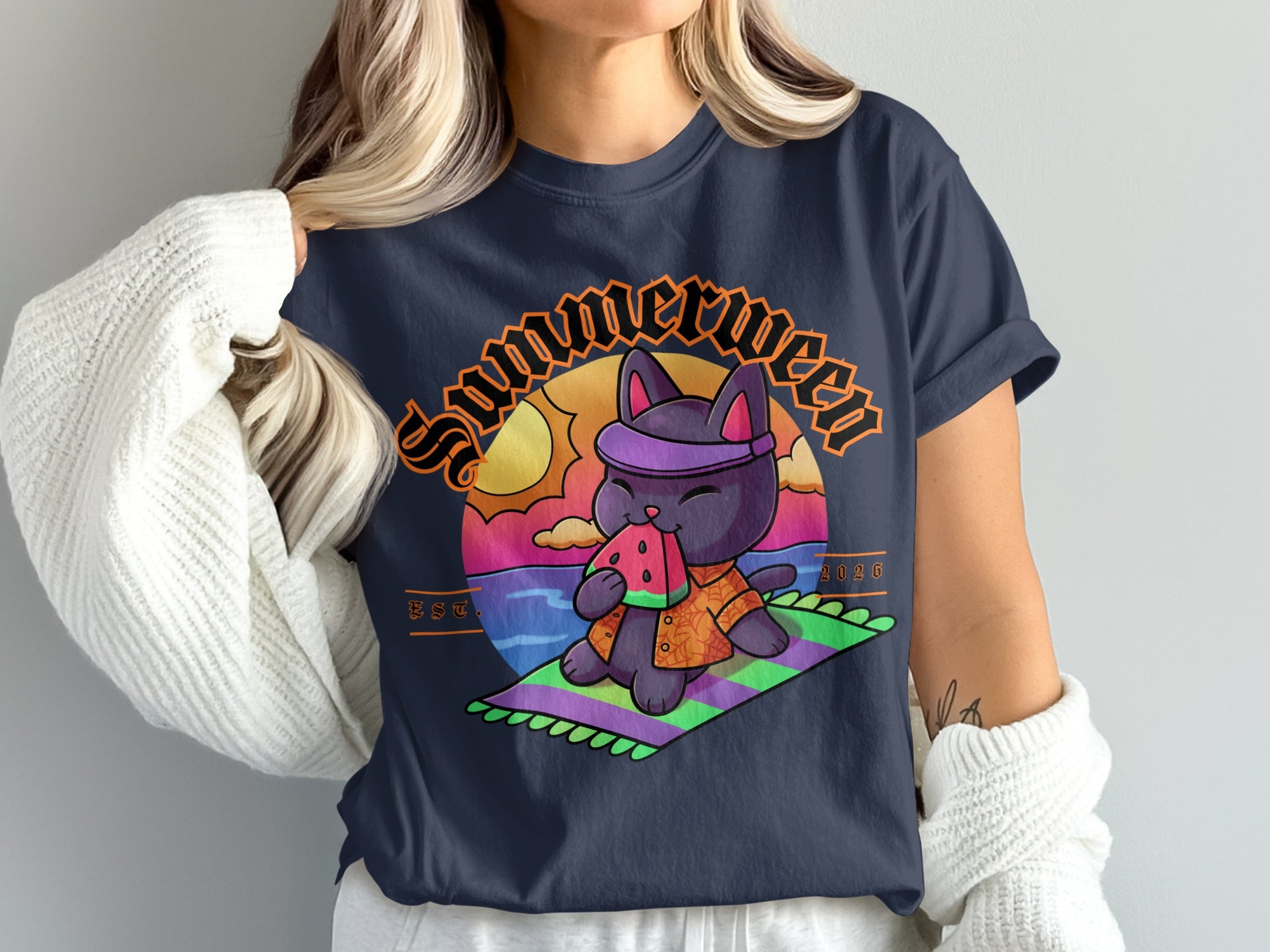 Black cat in bandana eating watermelon on a colorful blanket with sunset and water background.