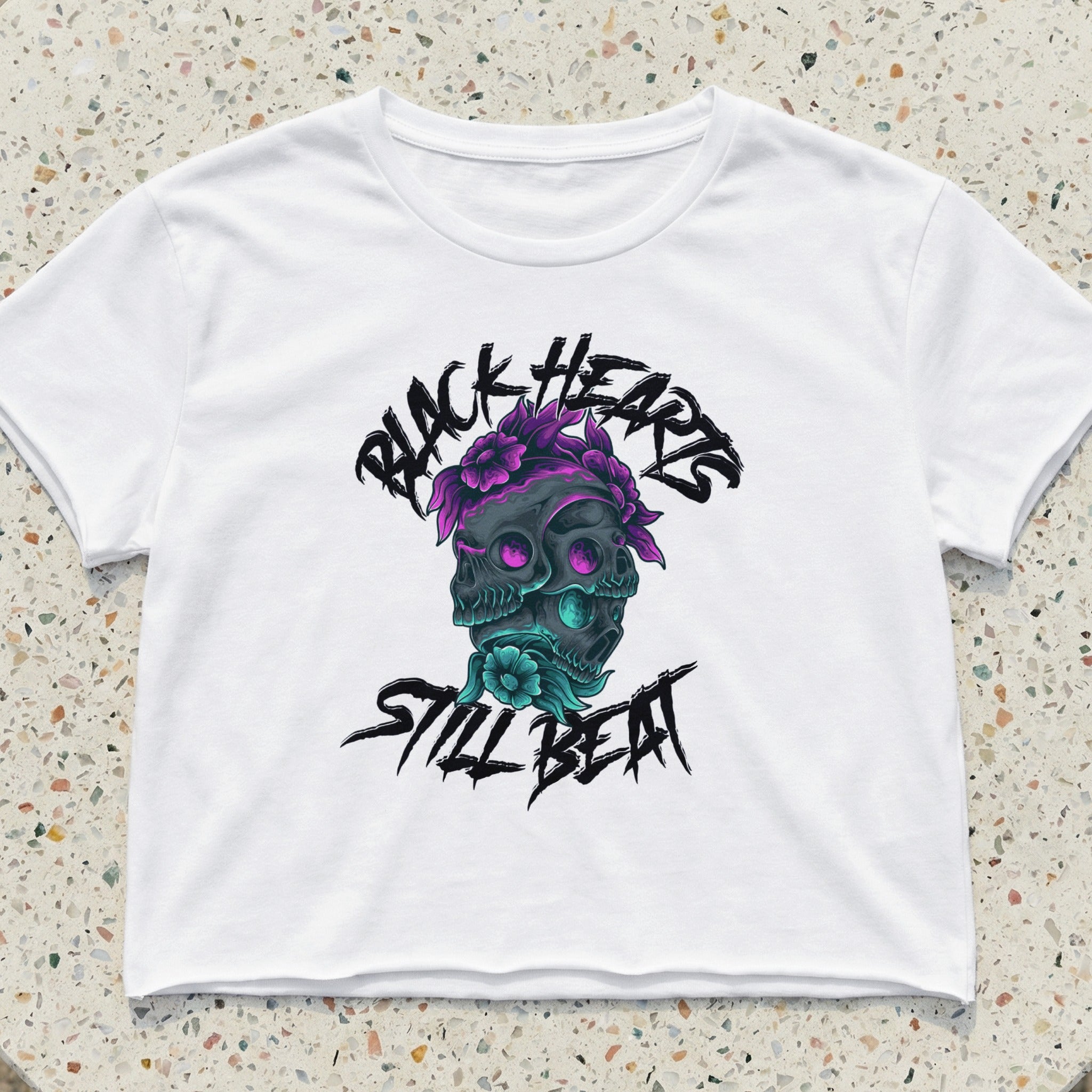 White crop top with black heart and skull graphic, flowers, and "Still Beat" text.