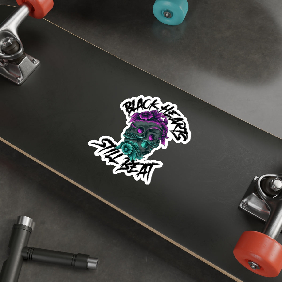 Black Hearts Still Beat skull sticker with purple flowers on skateboard.