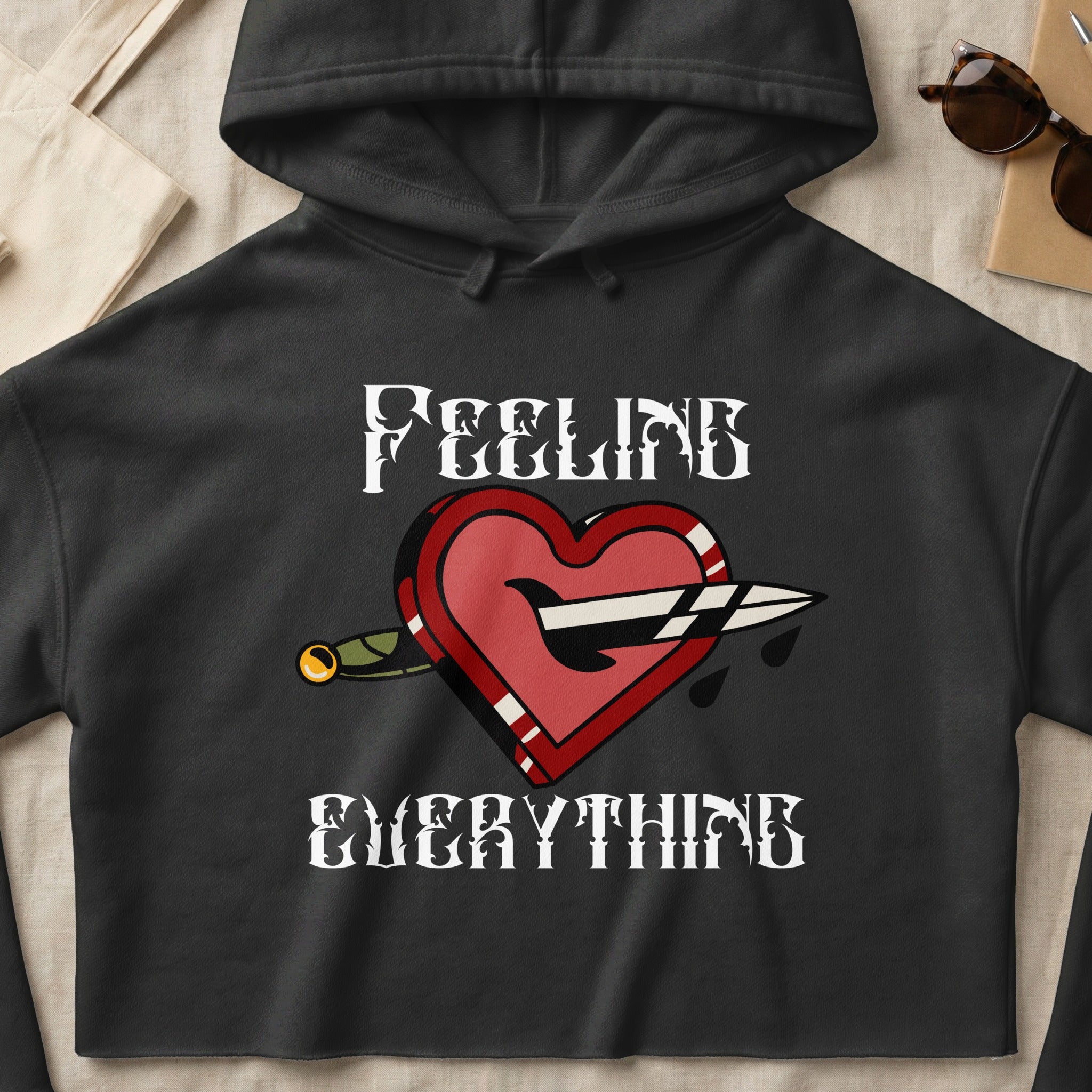 Black hoodie with stylized heart pierced by a dagger and text "FEELING EVERYTHING".