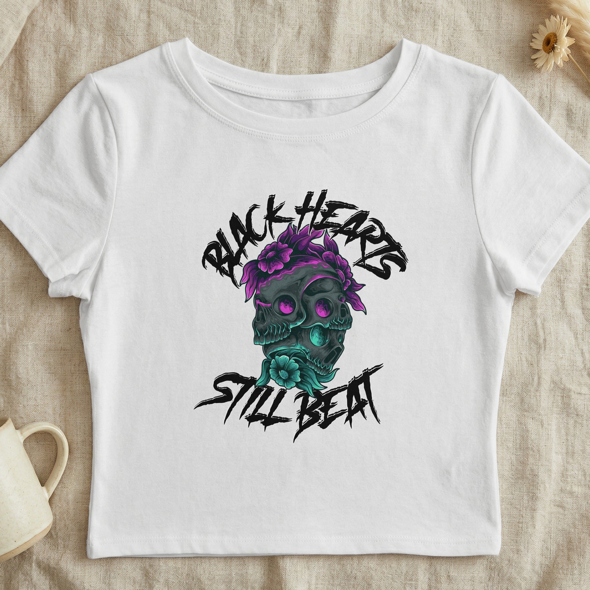 White cropped t-shirt with a skull and floral graphic that says "BLACK HEARTS STILL BEAT".