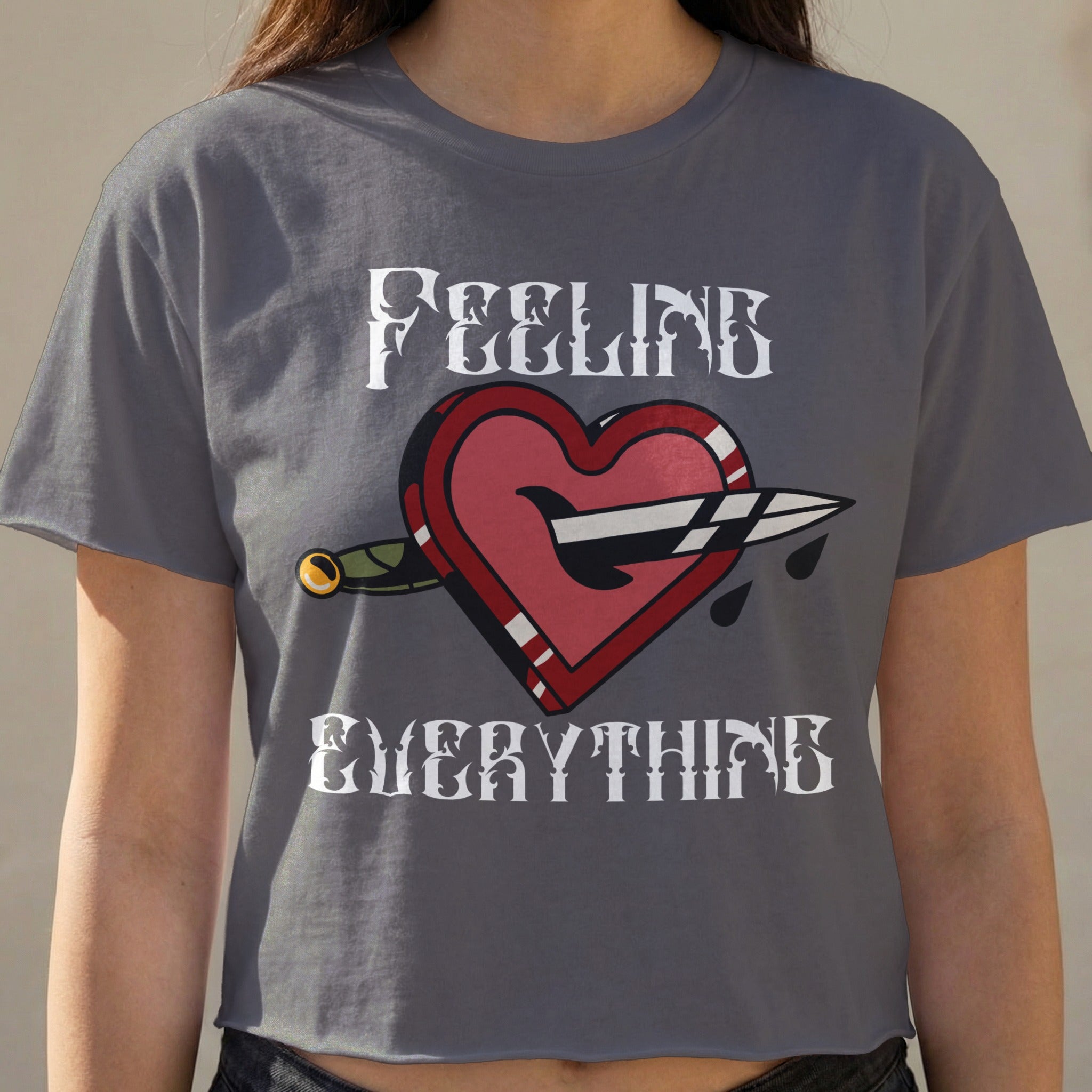 Cropped t-shirt with "FEELING EVERYTHING" text and a heart pierced by a dagger.
