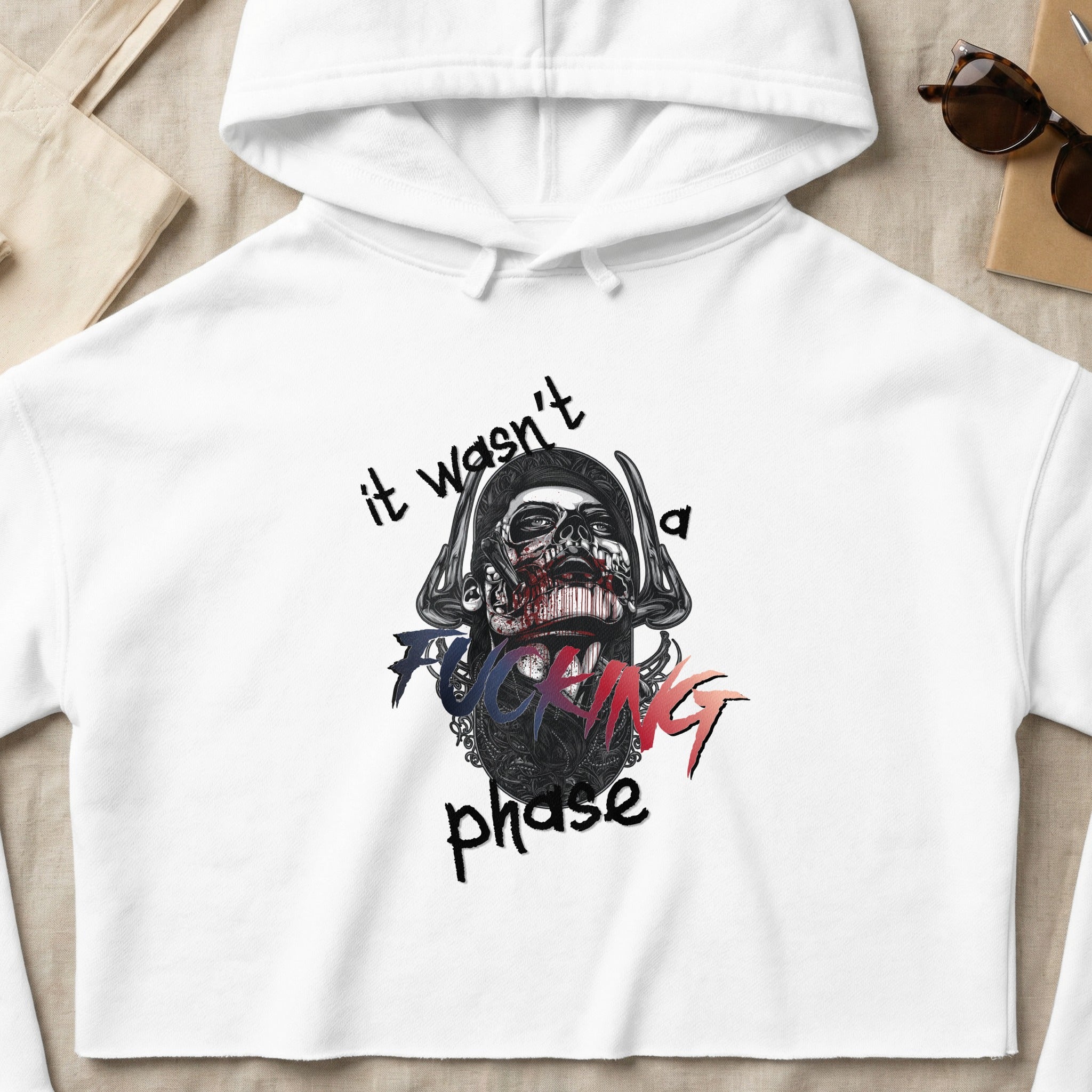 White crop hoodie with graphic of a skull with text "it wasn't a fucking phase".