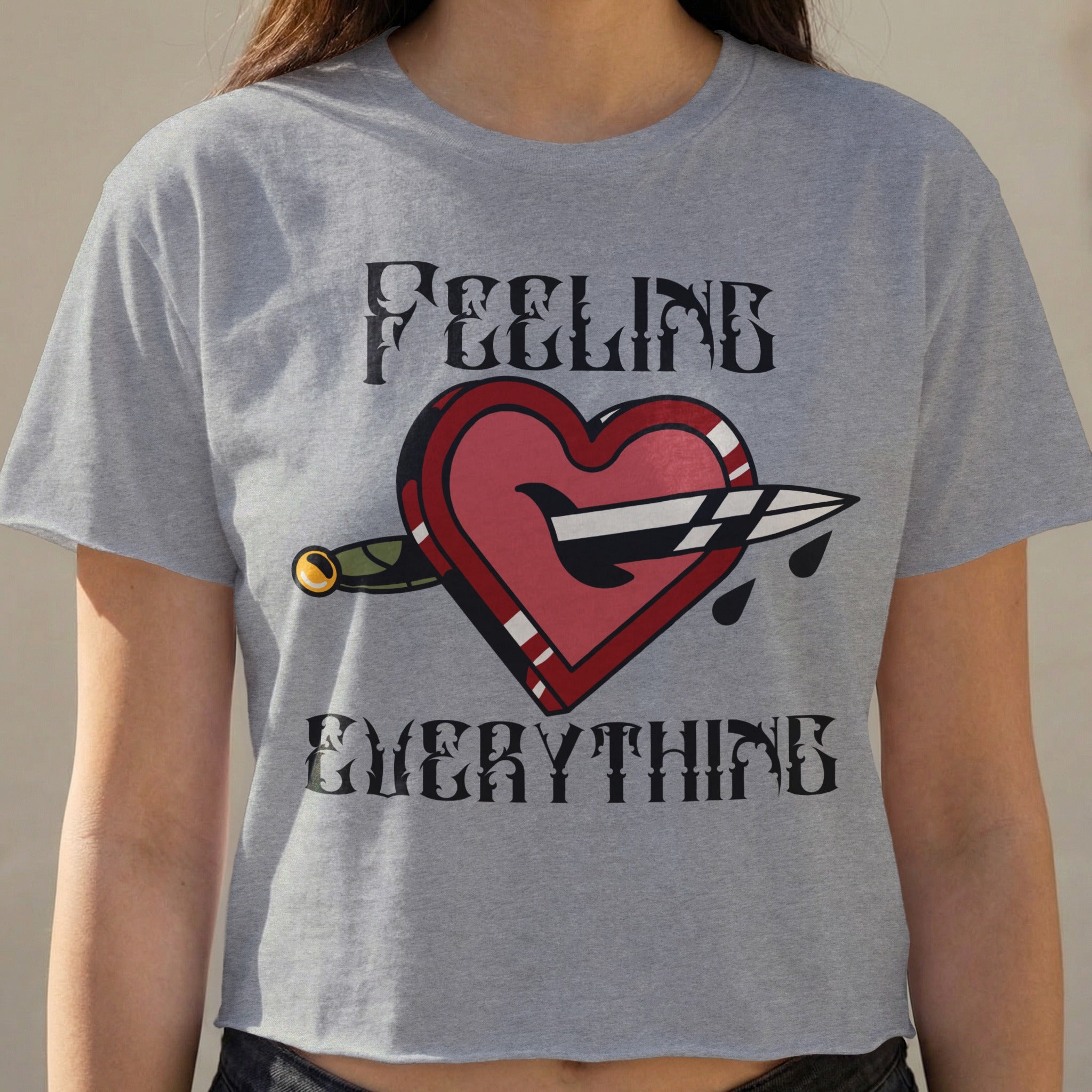 Grey crop top with "FEELING EVERYTHING" and a heart pierced by a knife.