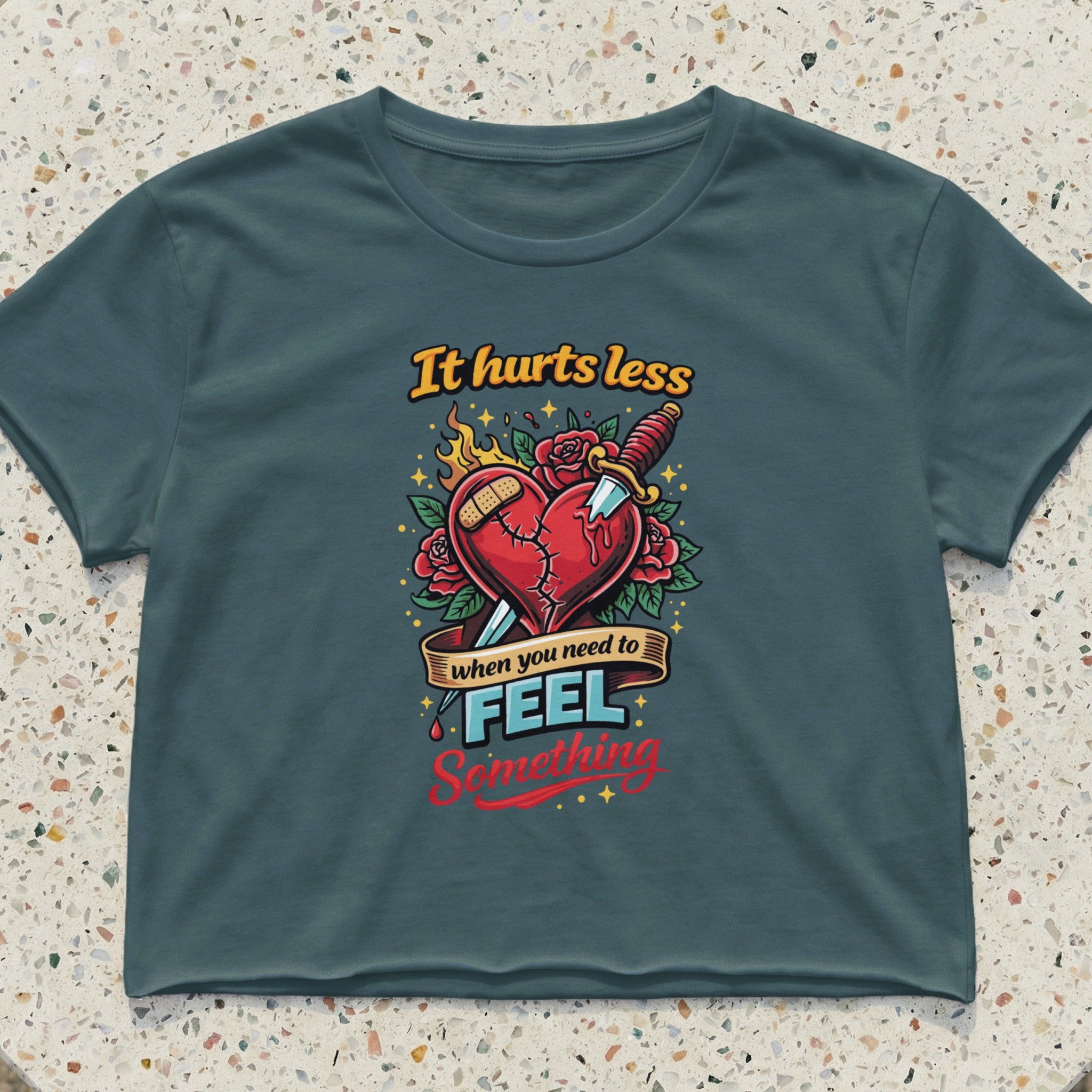 Crop top with a heart pierced by a knife and text "It hurts less when you need to feel something".