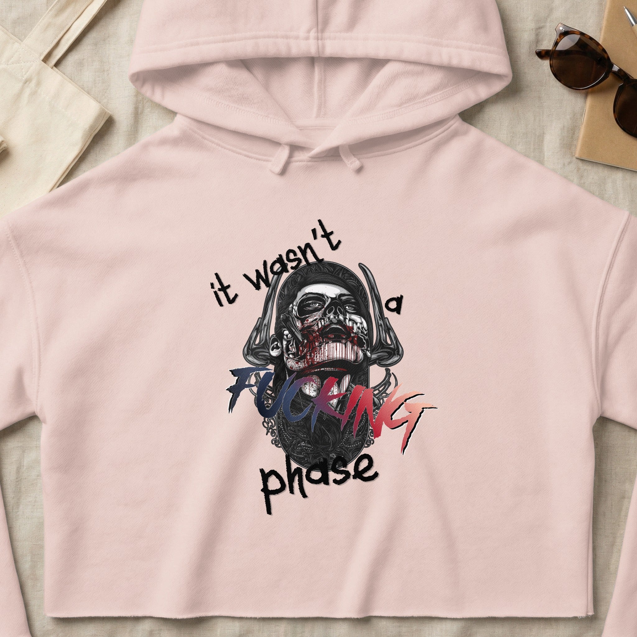 Pink cropped hoodie with skull graphic and "it wasn't a fucking phase" text.
