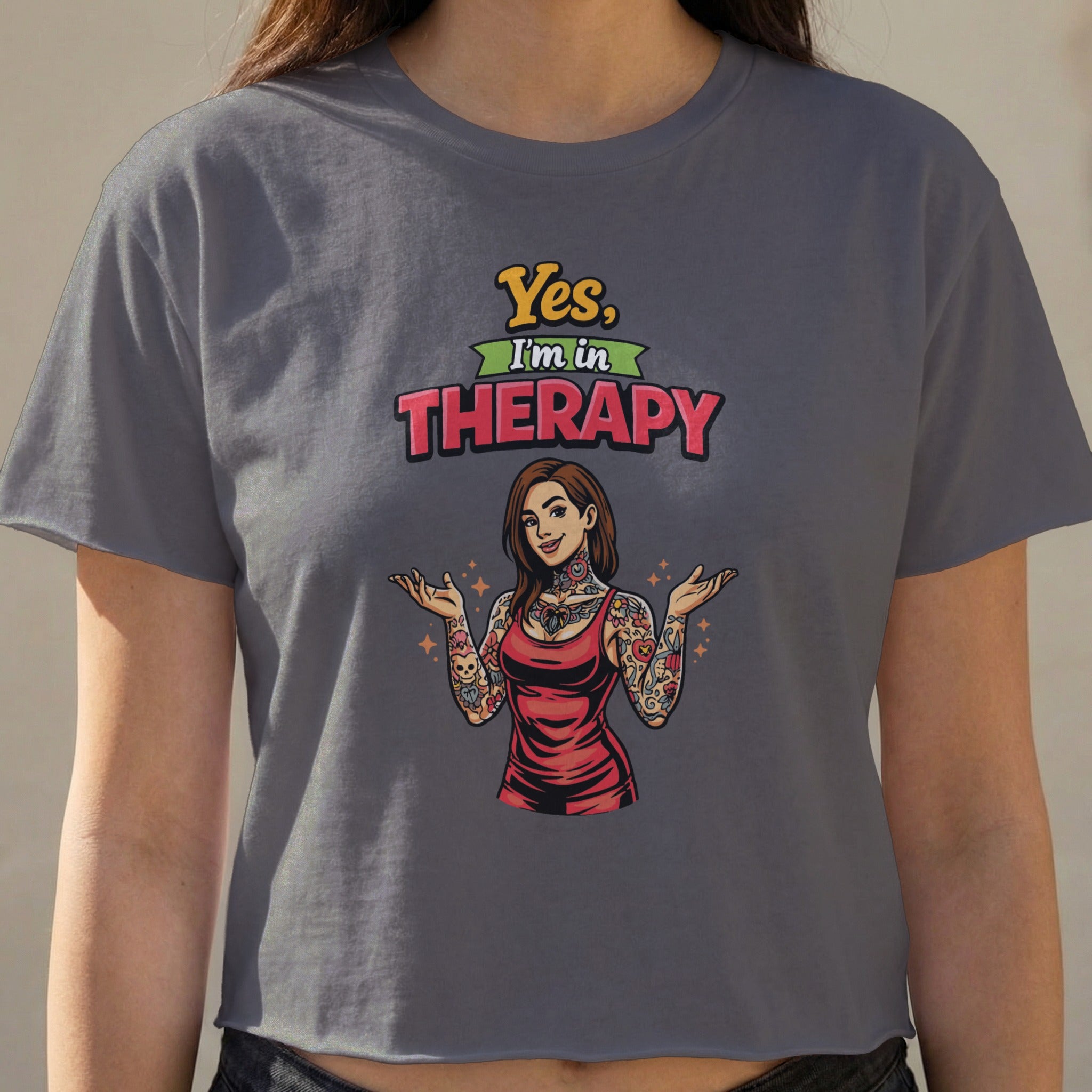 Woman wearing a gray cropped t-shirt with "Yes, I'm in Therapy" text and tattooed graphic.