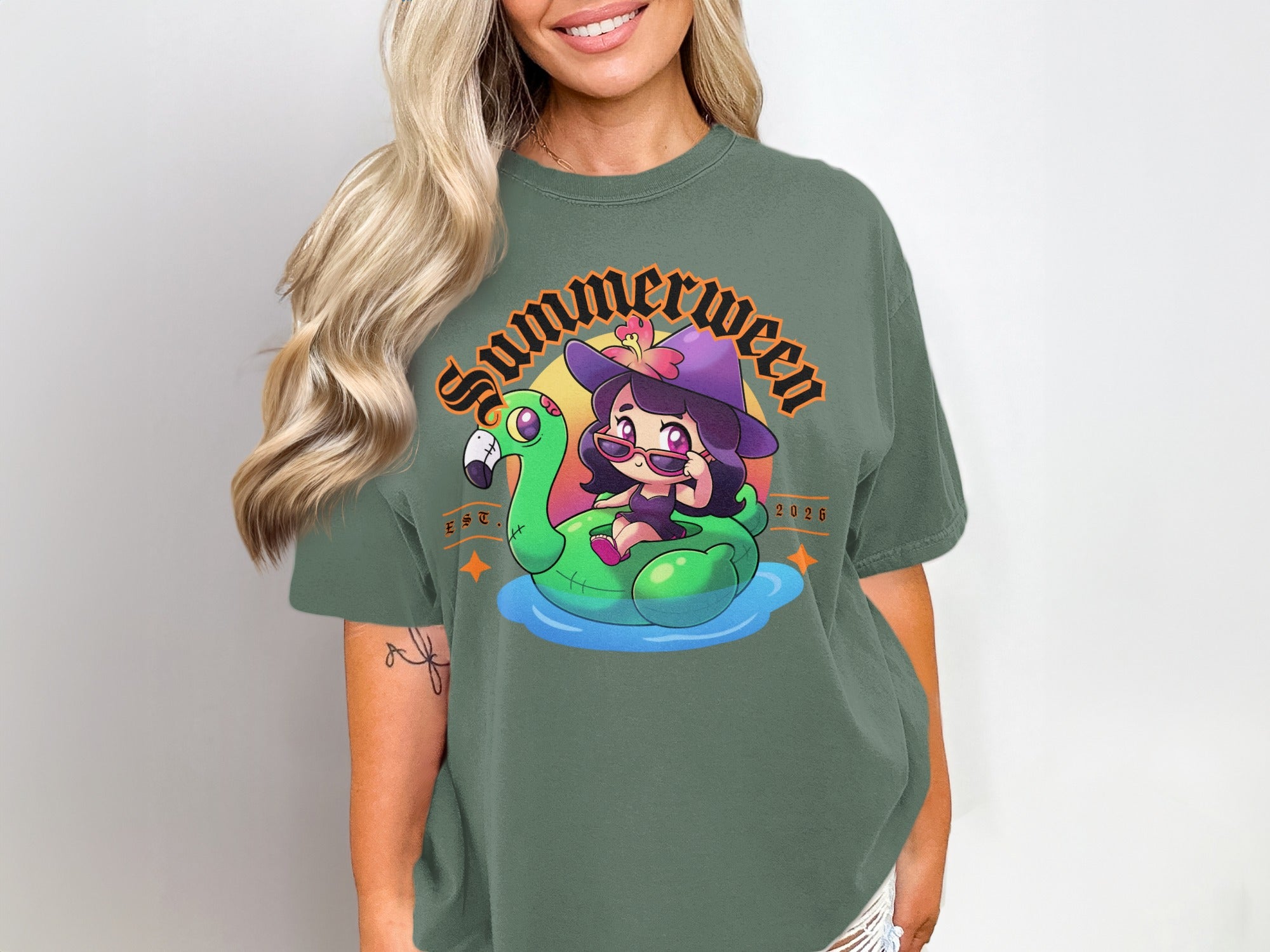 Green t-shirt graphic of a witch on a flamingo float with "Summerween Est. 2026" text.
