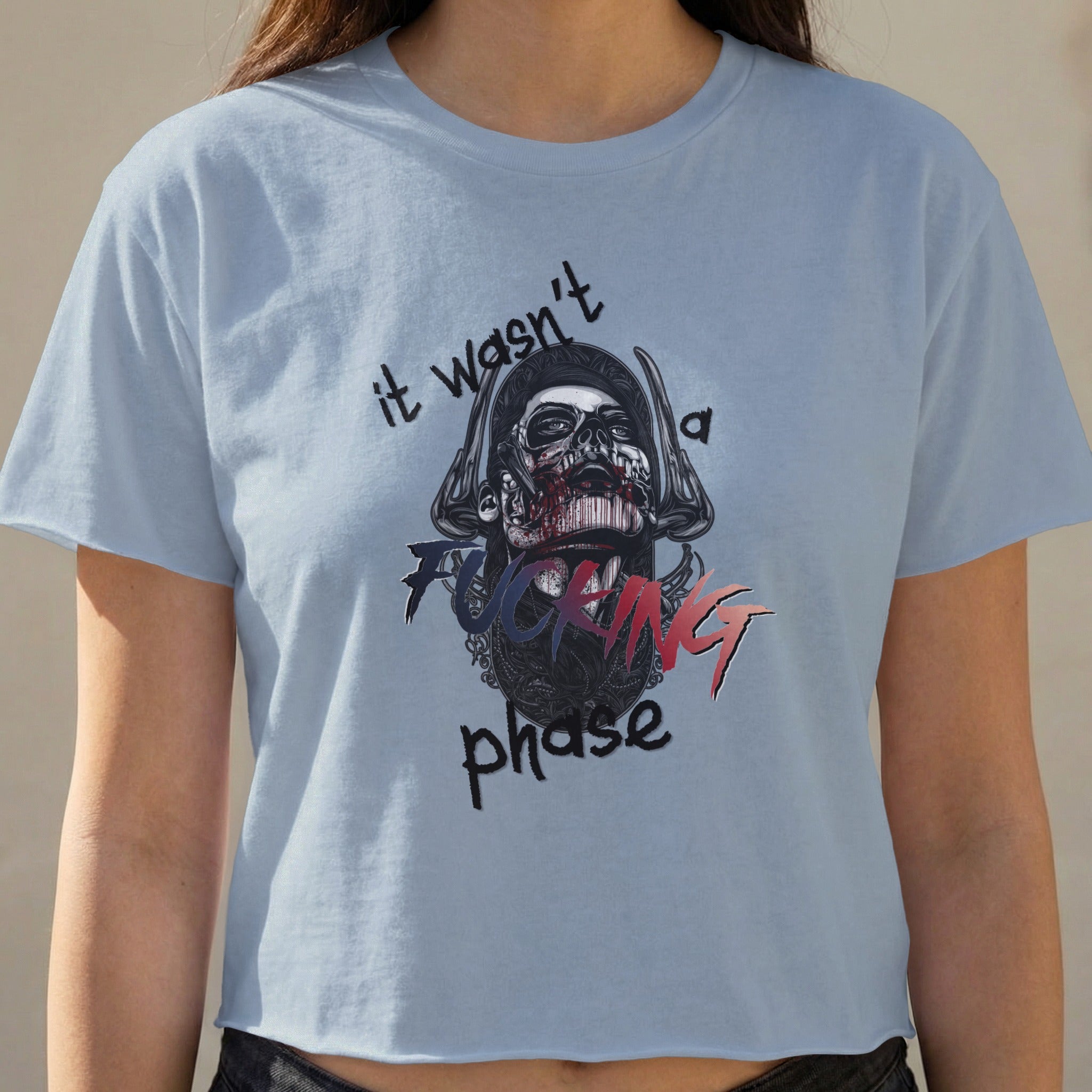 Light blue crop top with graphic of a skull wearing a helmet and text "it wasn't a fucking phase".