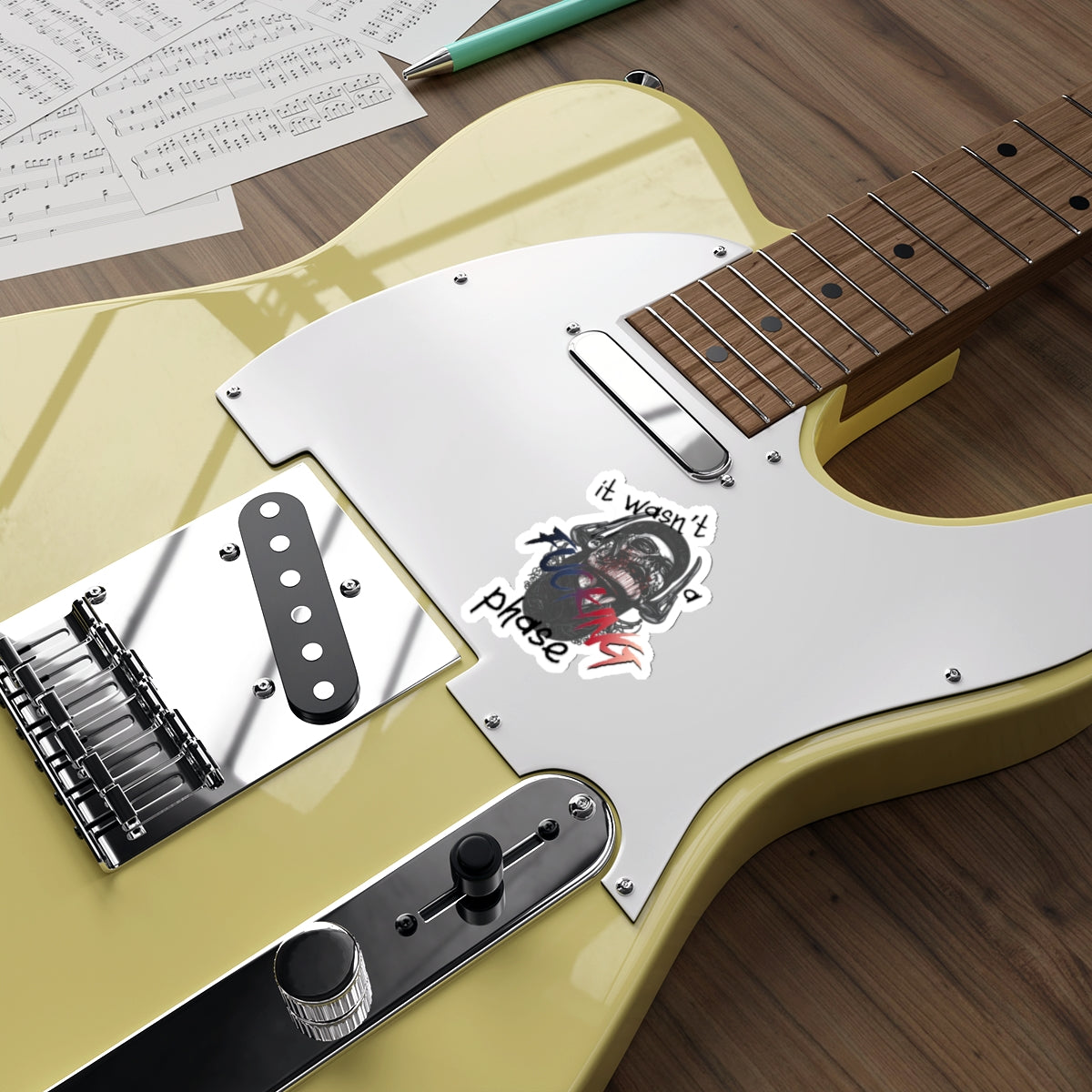 Guitar with "It wasn't a phase" sticker, sheet music, and pen.