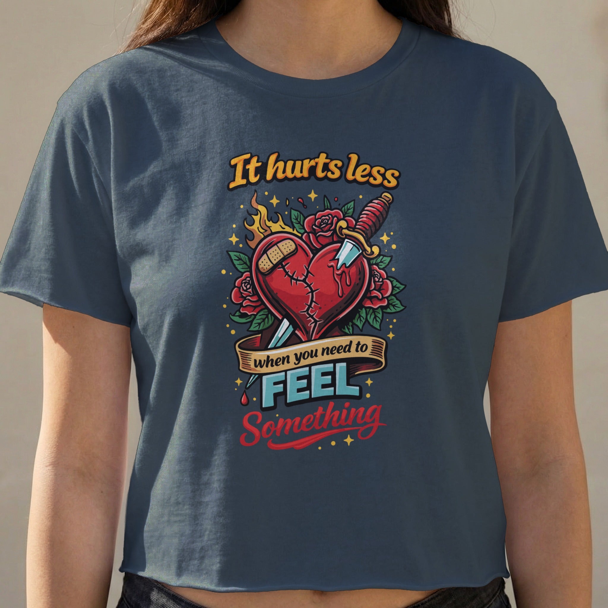 Dark t-shirt graphic with a broken heart stabbed by a knife, reading "It hurts less when you need to feel something."