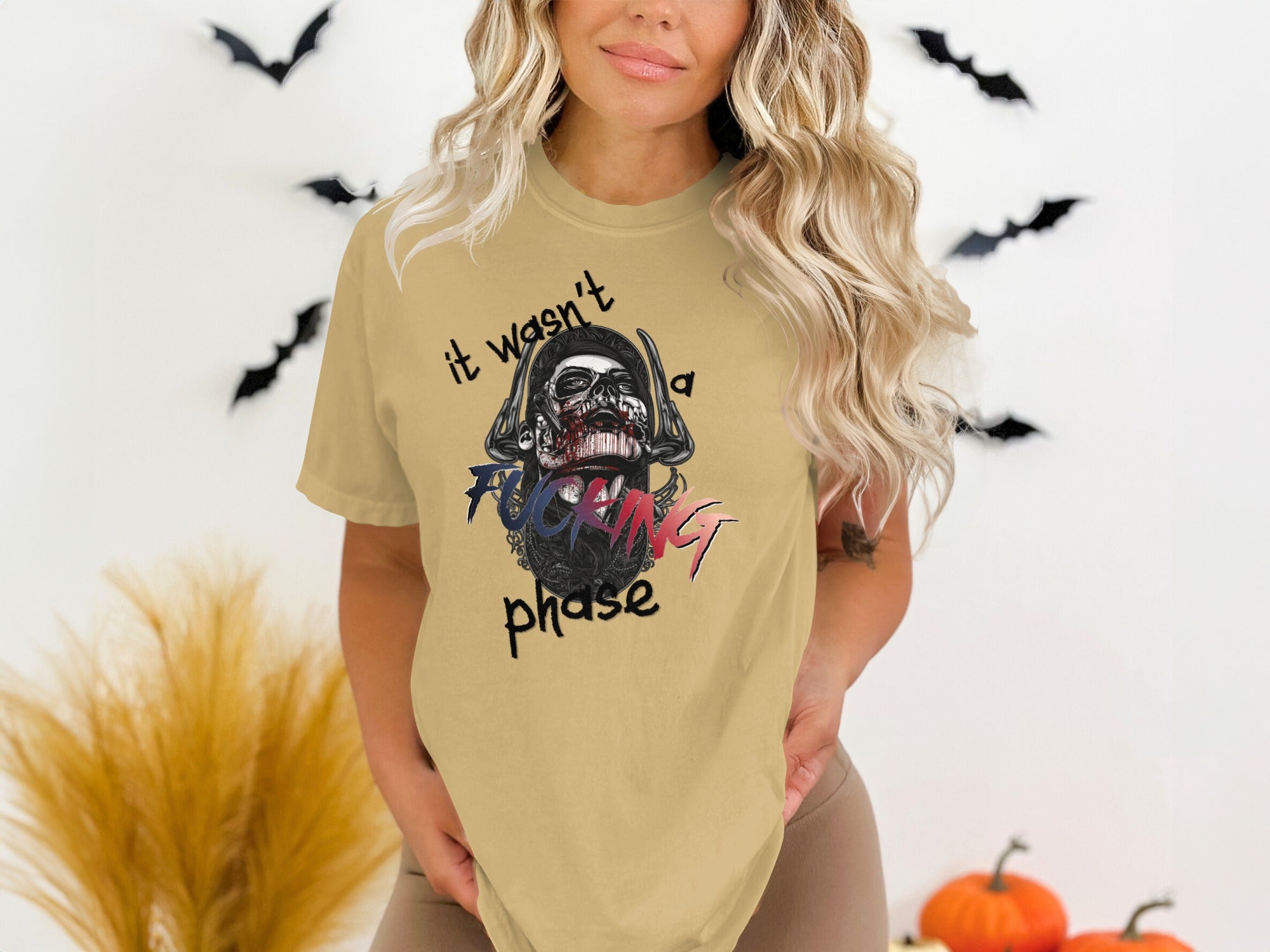 Woman wearing tan t-shirt with skull graphic and text.