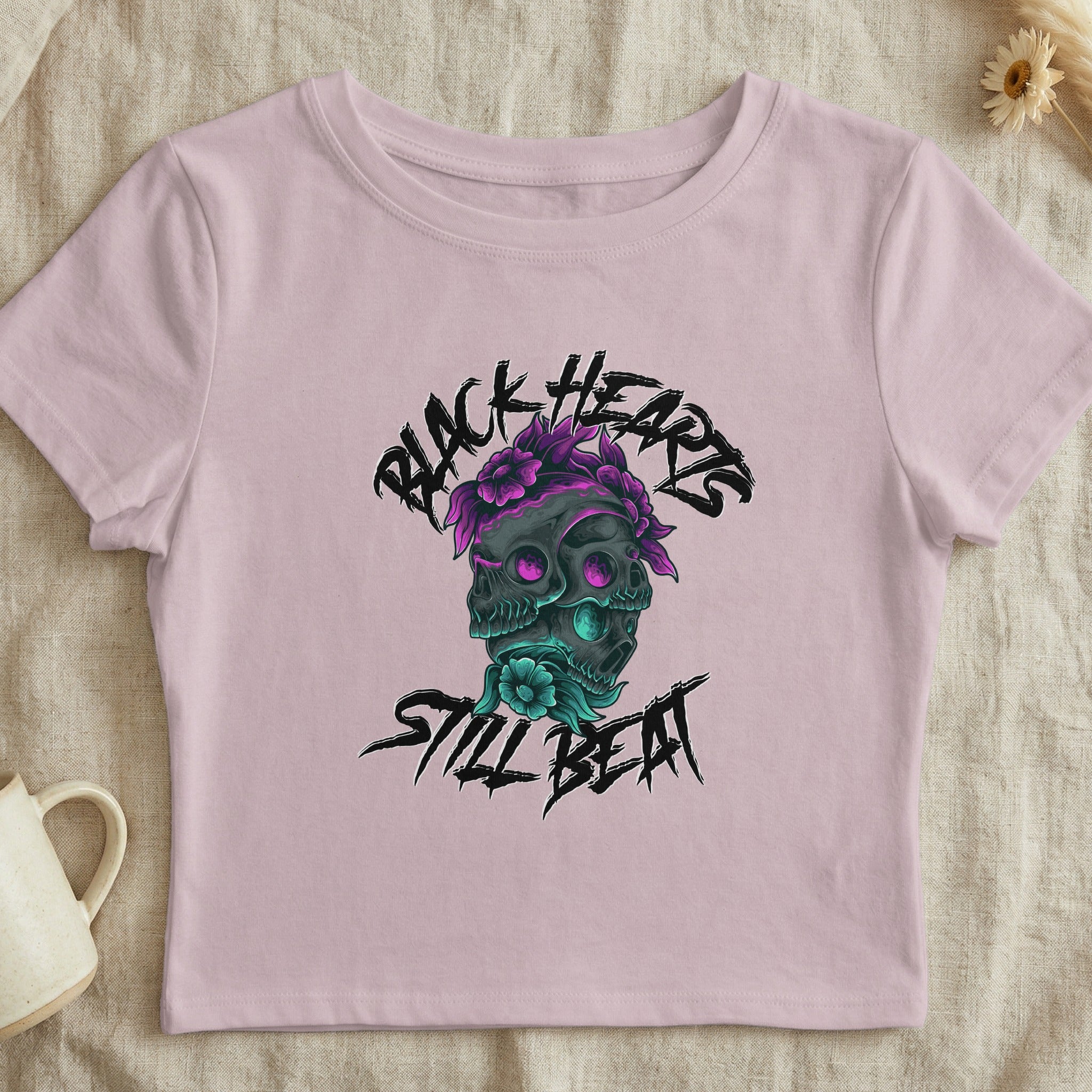 Pink crop top with black hearts, skull, and floral graphic and text.
