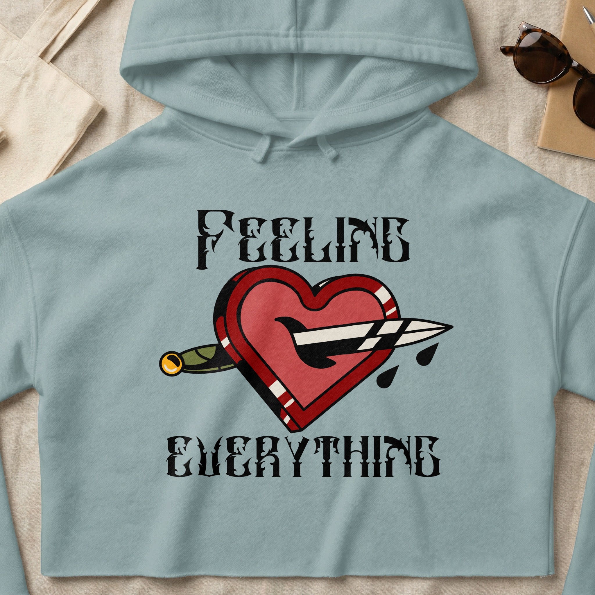 Light blue hoodie with dagger through heart graphic and "Feeling Everything" text.