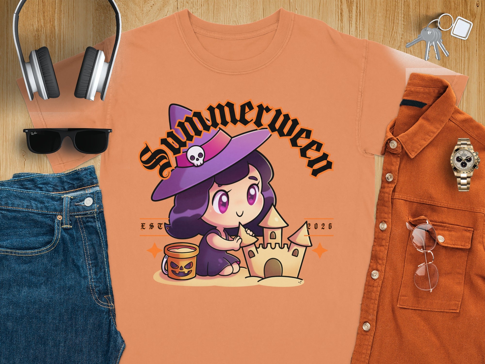Cute witch with sandcastle on orange t-shirt, text "Summerween EST 2026".