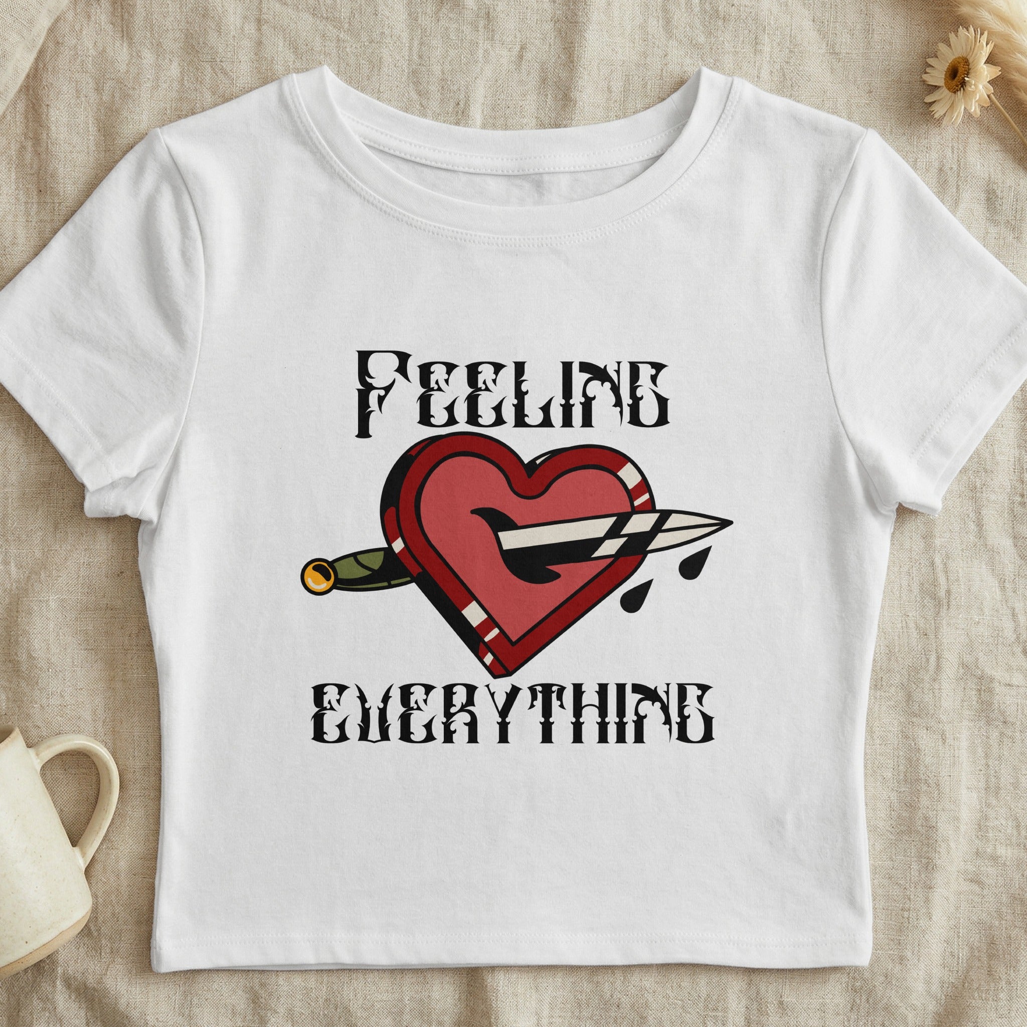 White cropped t-shirt with heart pierced by knife graphic and text "FEELING EVERYTHING".