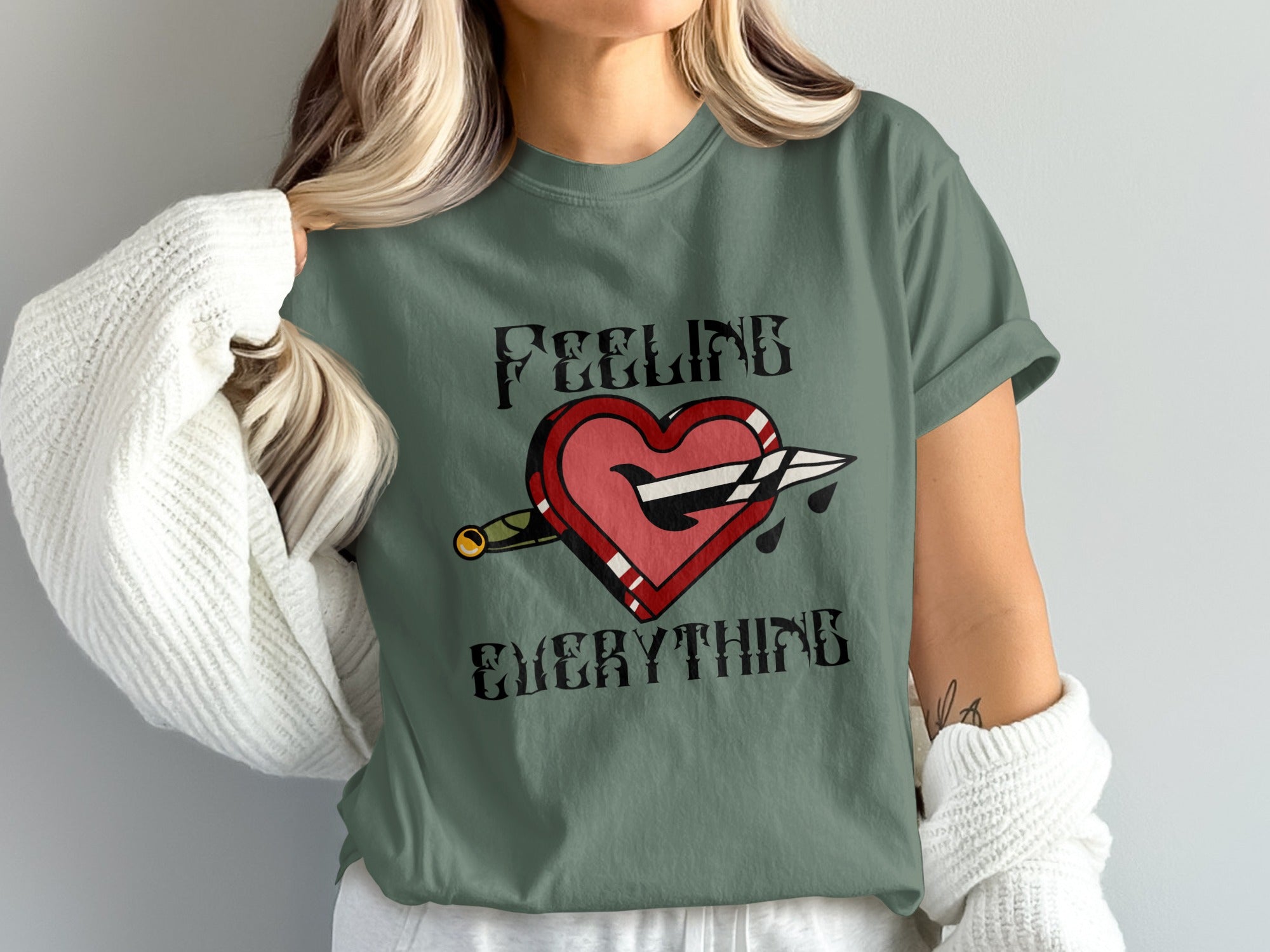 Green t-shirt with a heart pierced by a dagger, text "FEELING EVERYTHING".