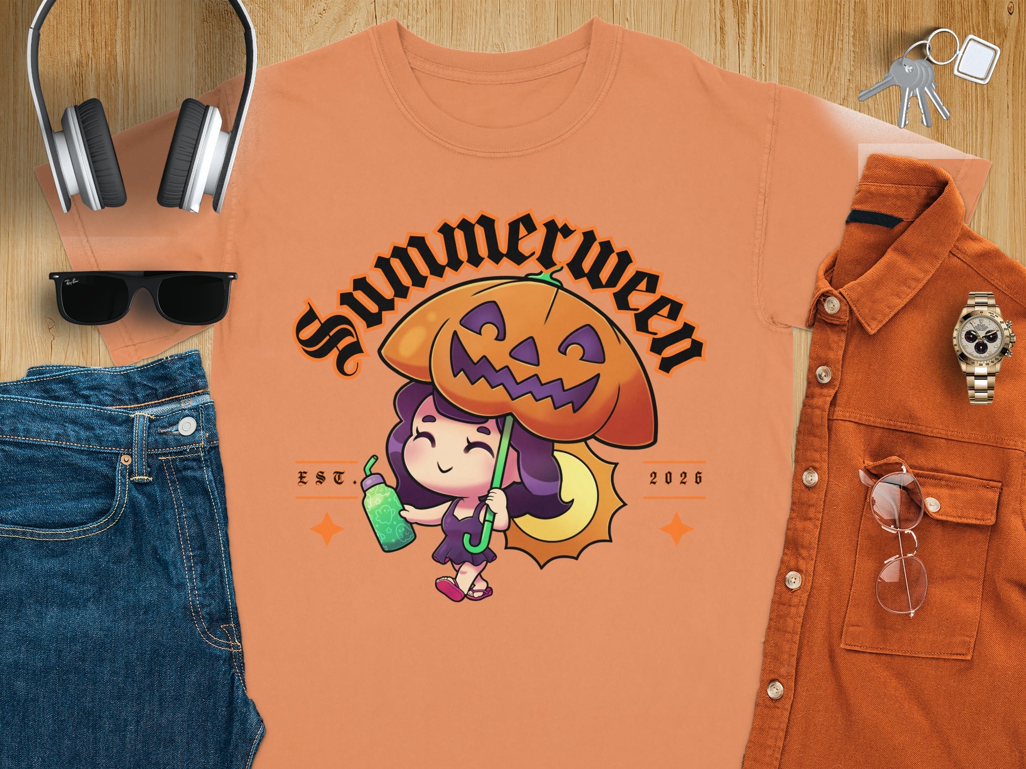 Peach t-shirt with a "Summerween" graphic of a girl holding a drink under a pumpkin umbrella.