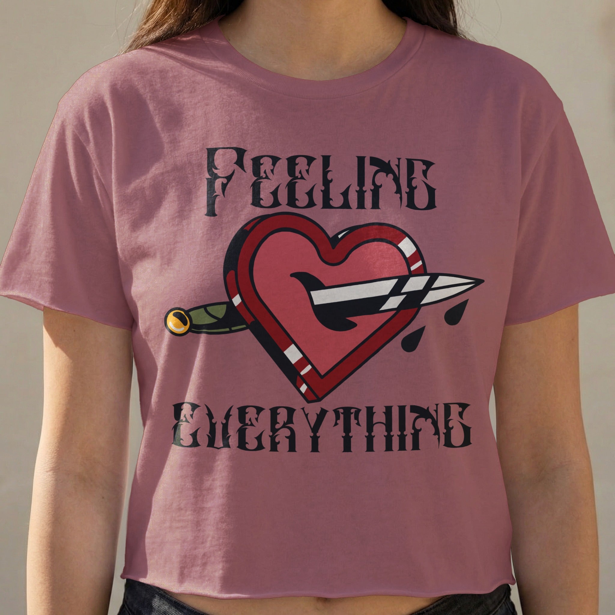 Pink t-shirt with a heart stabbed by a dagger and the words "FEELING EVERYTHING".