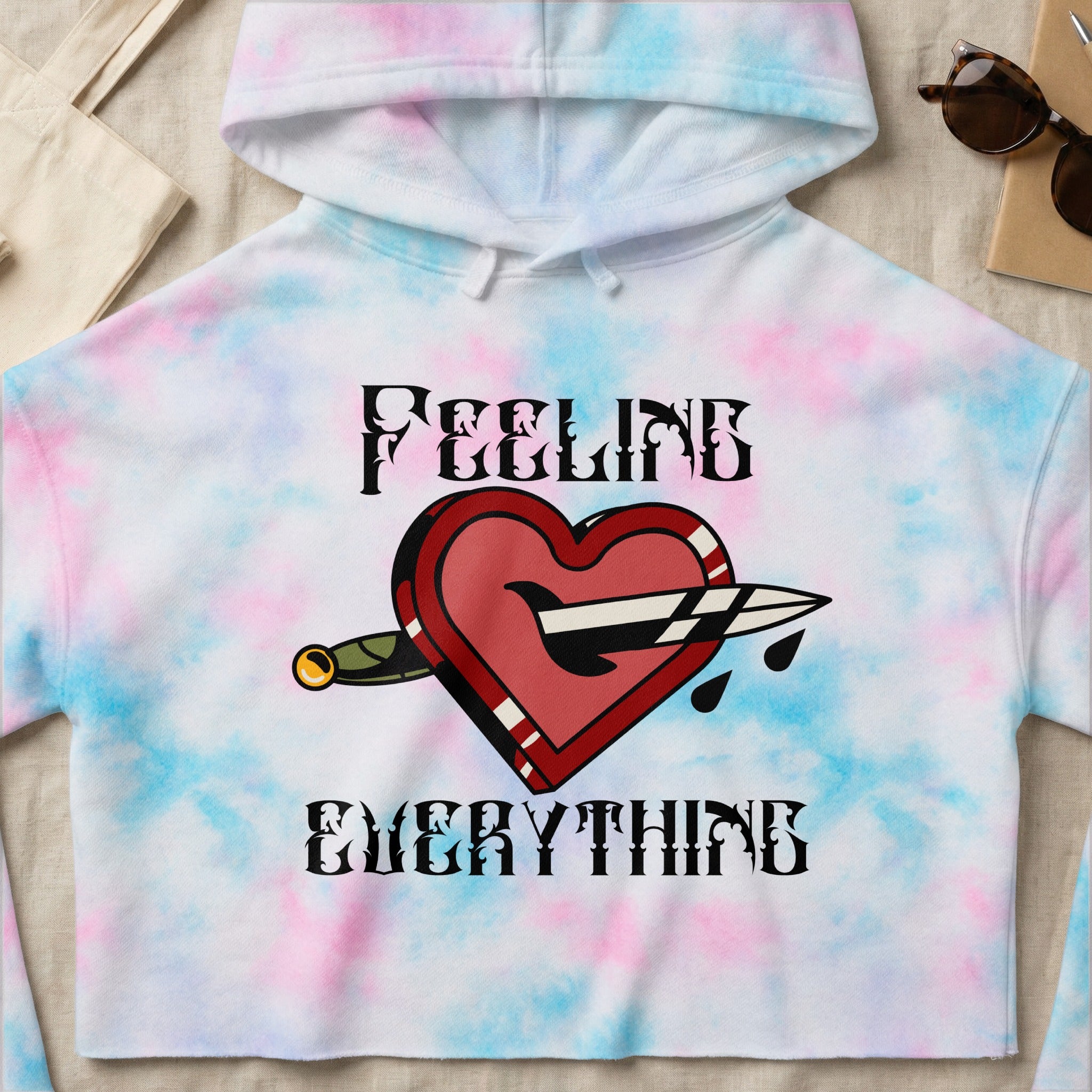 Crop hoodie with tie-dye pattern and heart with dagger graphic and text "FEELING EVERYTHING".