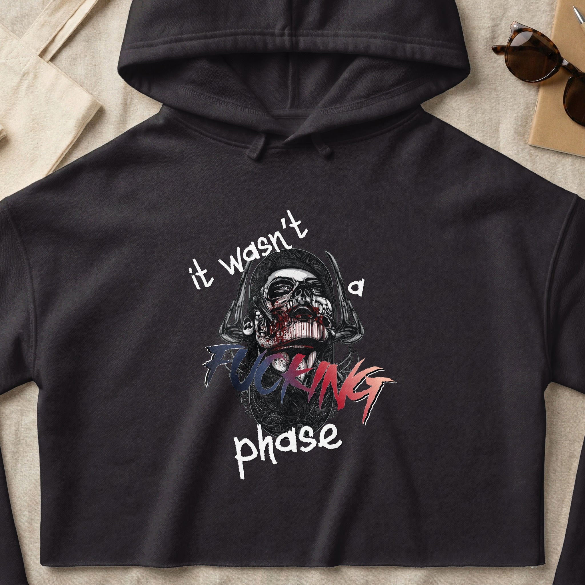 Black hoodie with a graphic of a skull with text "it wasn't a fucking phase".