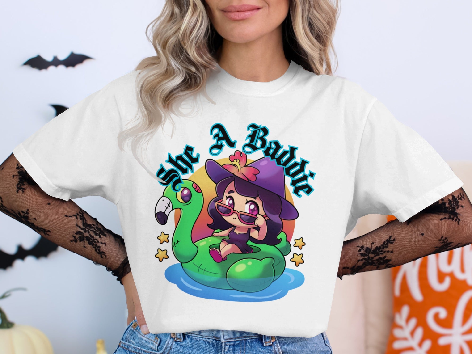 White t-shirt graphic with a witch on a flamingo float saying "She A Baddie".