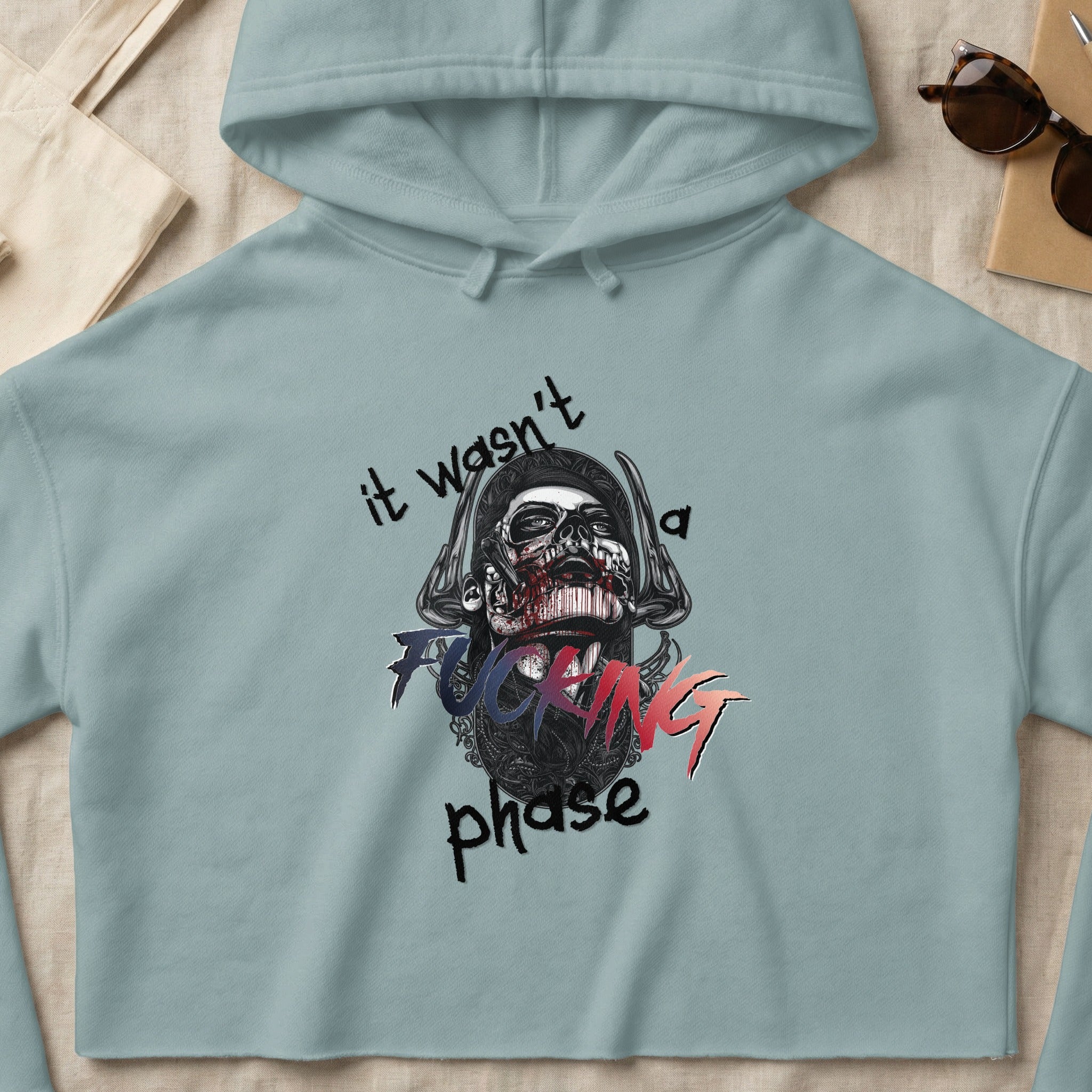Light blue cropped hoodie with graphic of a skull and text "it wasn't a fucking phase".