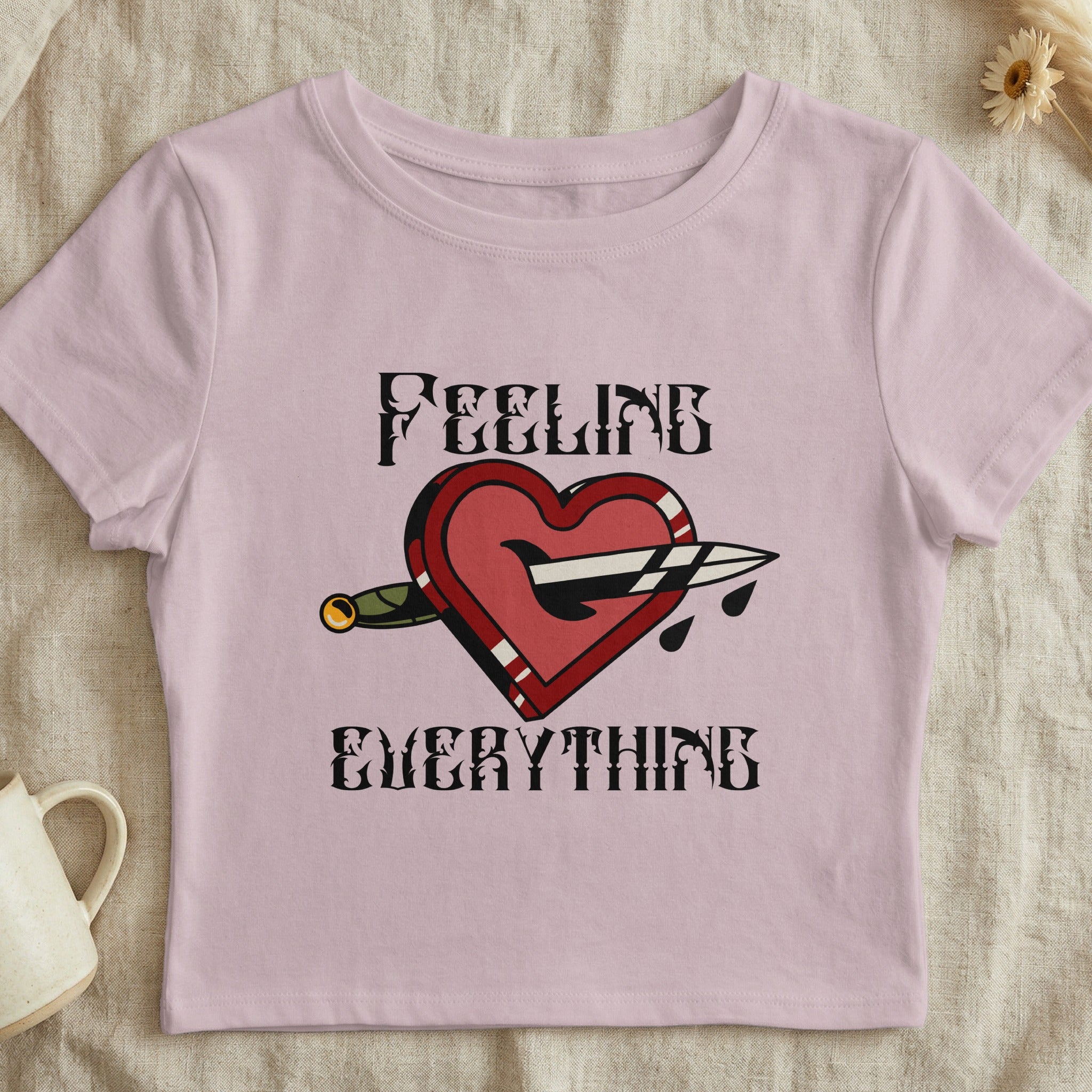 Pink t-shirt with heart pierced by dagger and text "FEELING EVERYTHING".