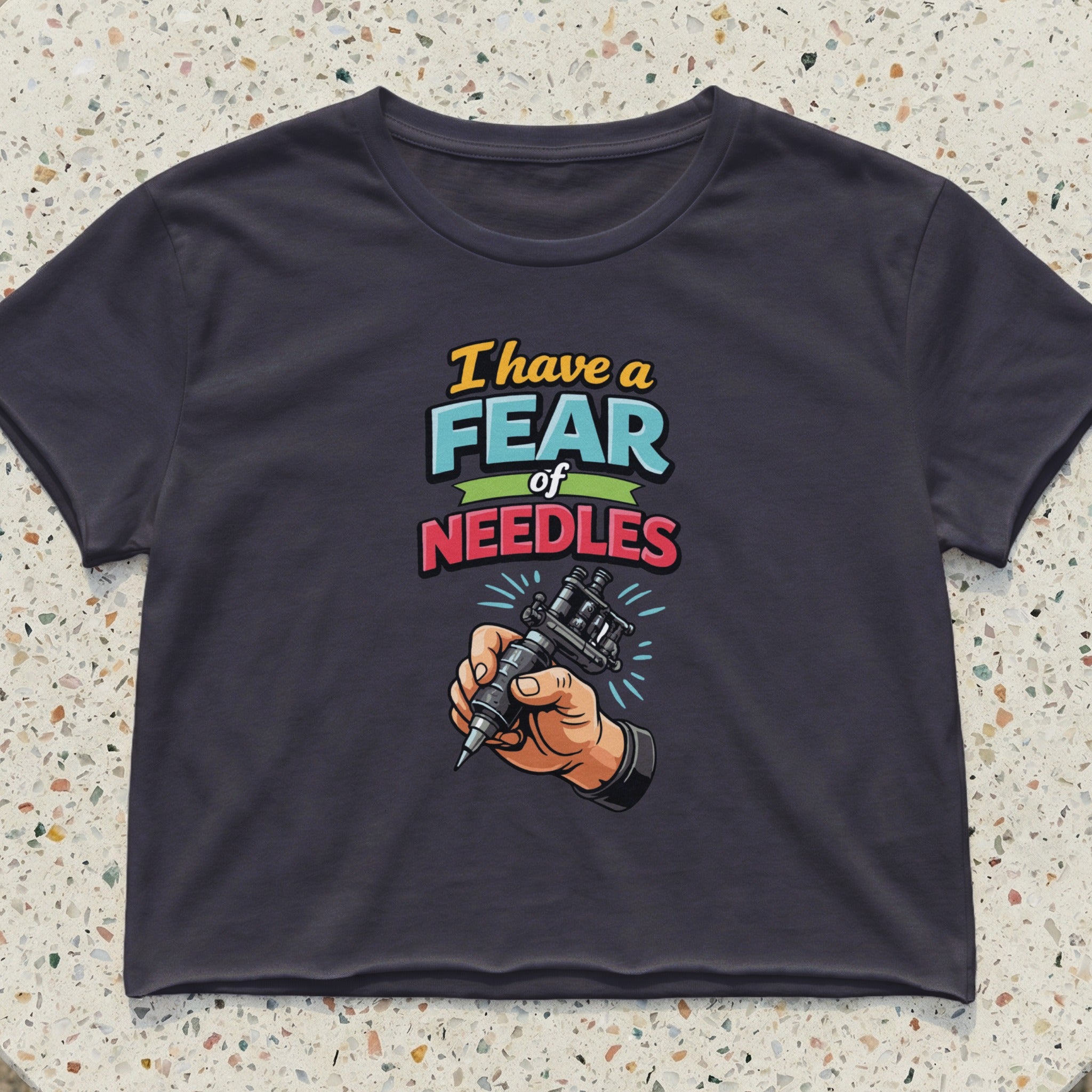 Dark crop top with "I have a fear of NEEDLES" text and hand holding tattoo gun.