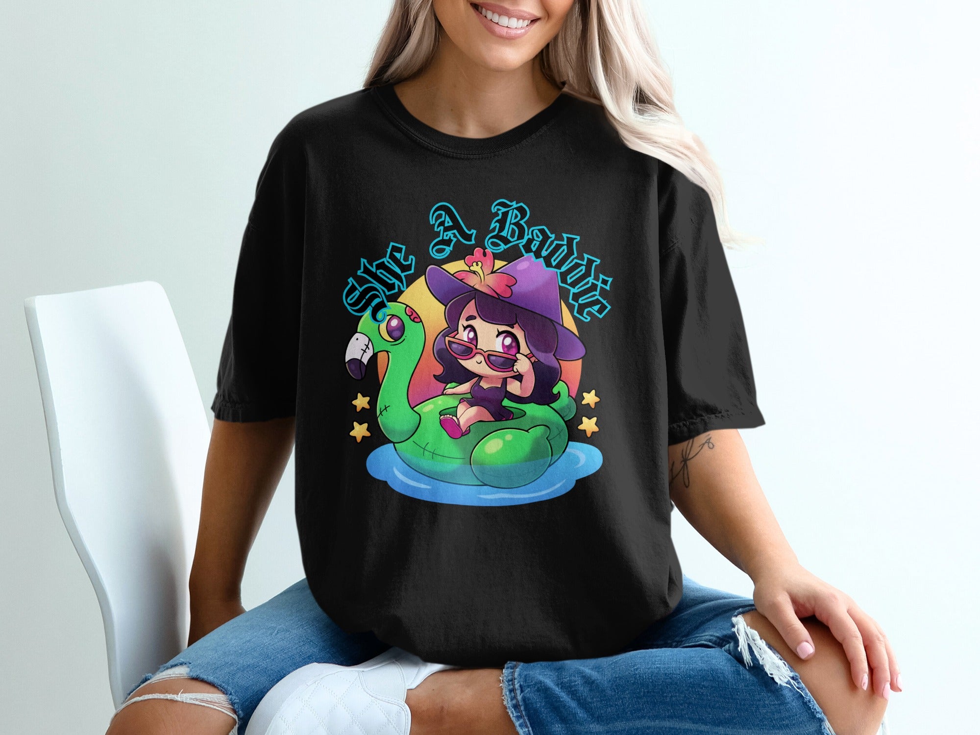 Black t-shirt with "She A Baddie" text and cartoon witch on flamingo float.