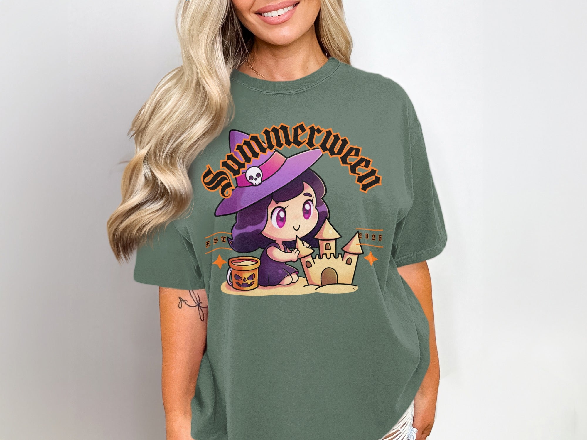 Green t-shirt with a cartoon witch building a sandcastle, with text "Summerween 2026".