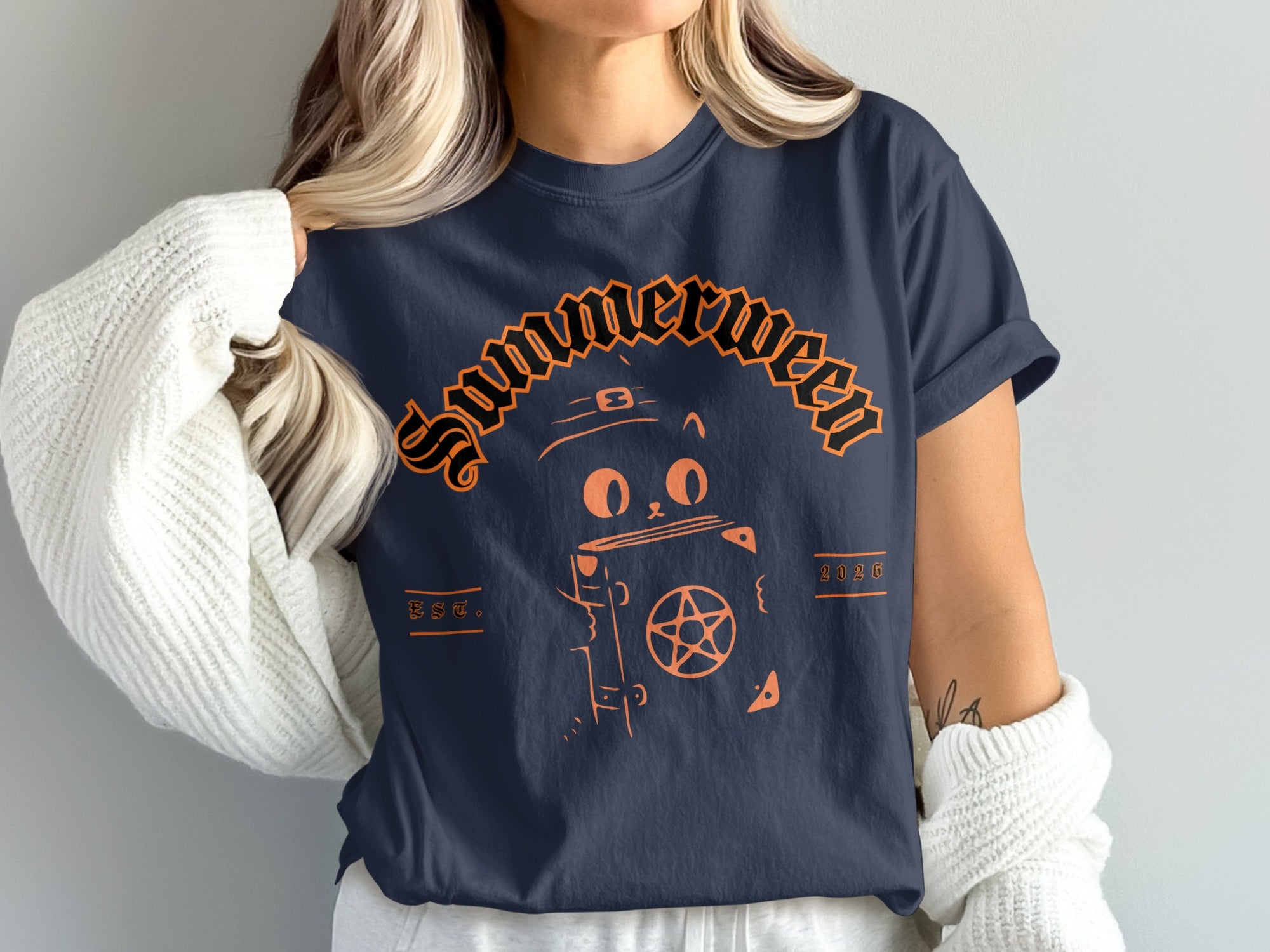 Navy t-shirt with orange graphic of a cat wearing a witch hat holding a book with a pentagram.