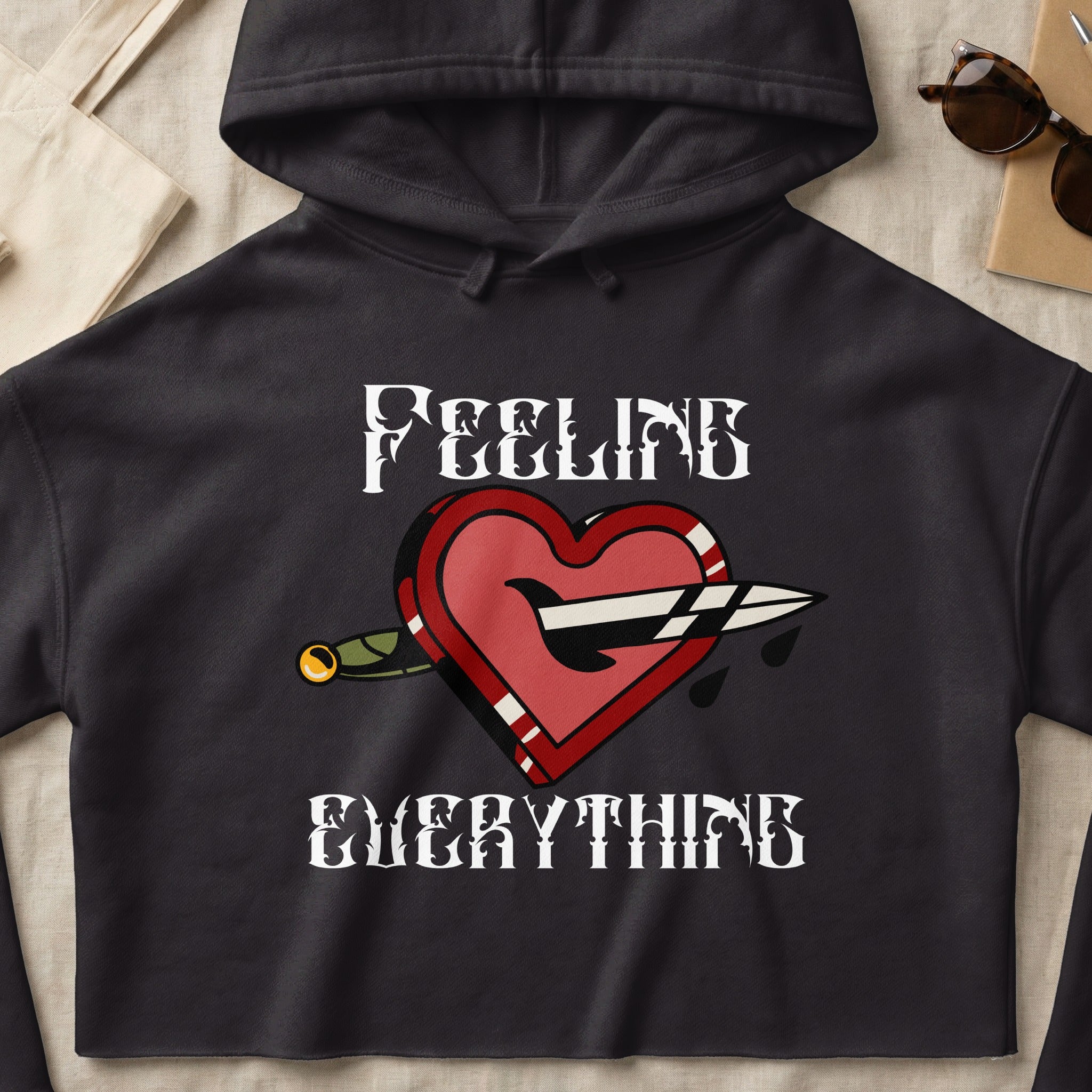 Black hoodie with red heart pierced by a dagger and text "FEELING EVERYTHING".