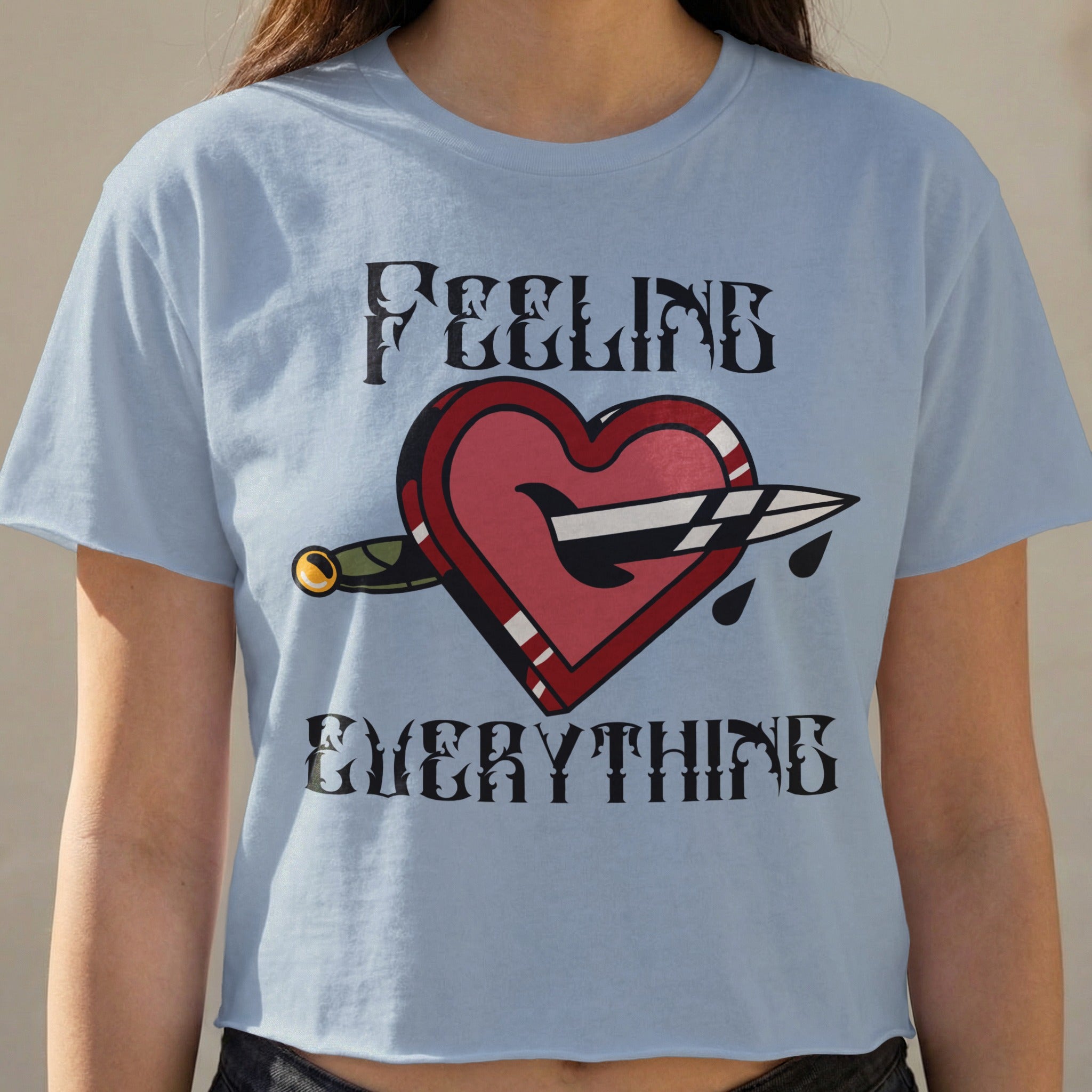 Light blue t-shirt with a red heart pierced by a dagger and "FEELING EVERYTHING" text.