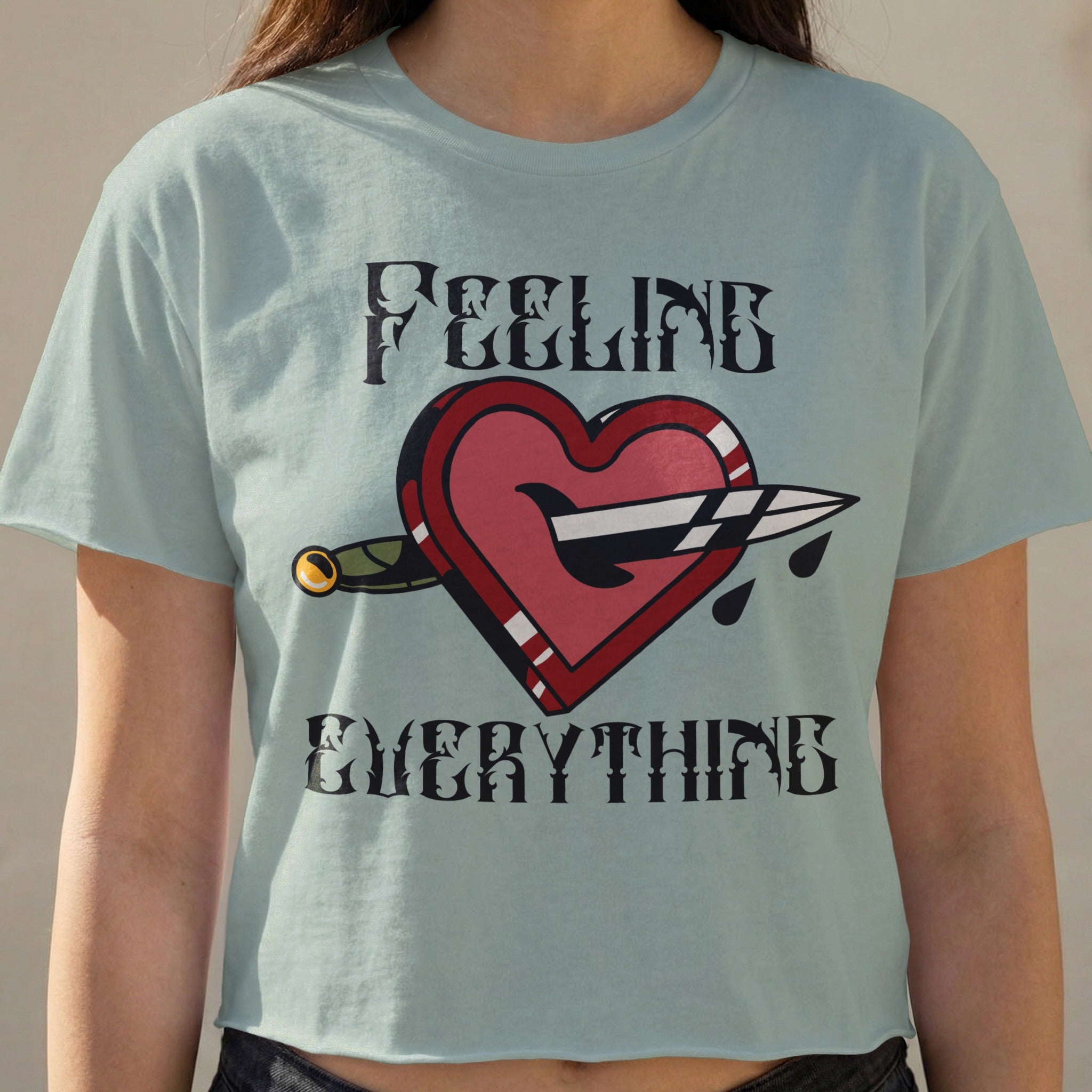 Light blue crop top with a heart pierced by a dagger and "FEELING EVERYTHING" text.